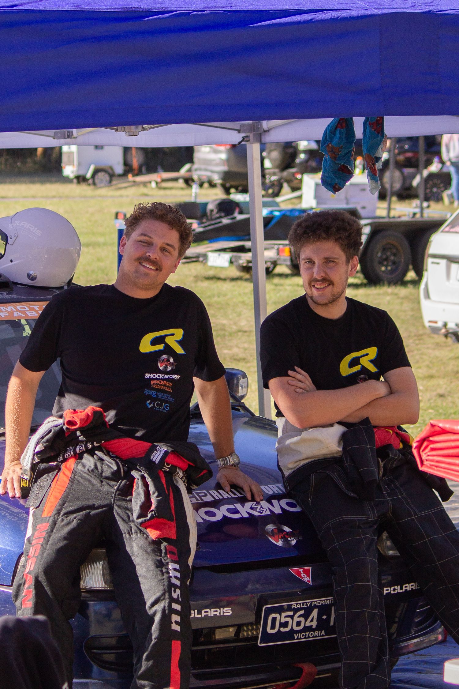 Racing team members gathered under a blue canopy tent with equipment and gear.