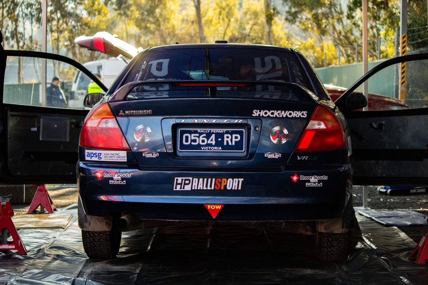 Rear view of blue rally car with racing decals in service area.