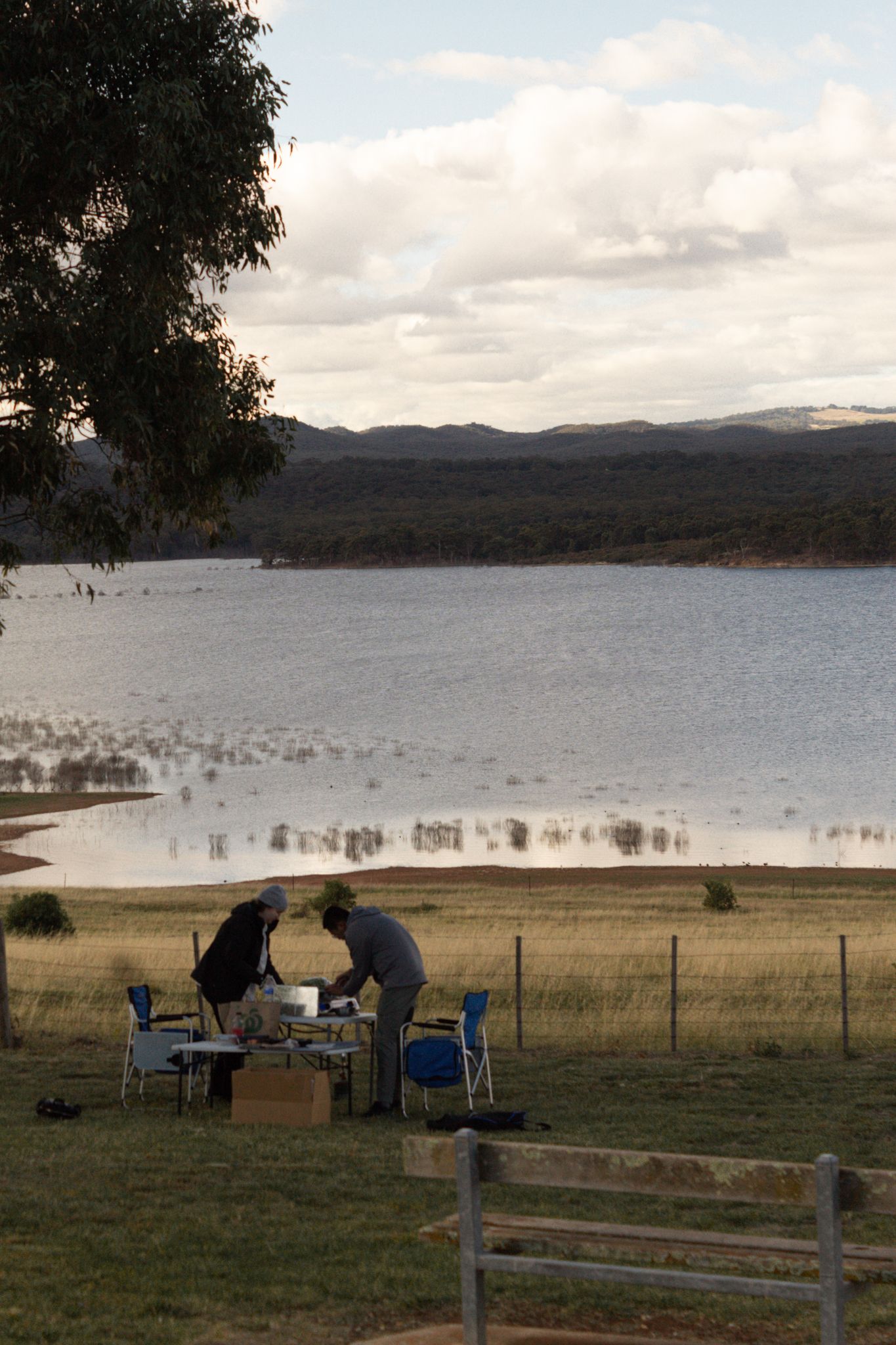 Lakeside campsite setup with chairs and equipment against a mountain backdrop.