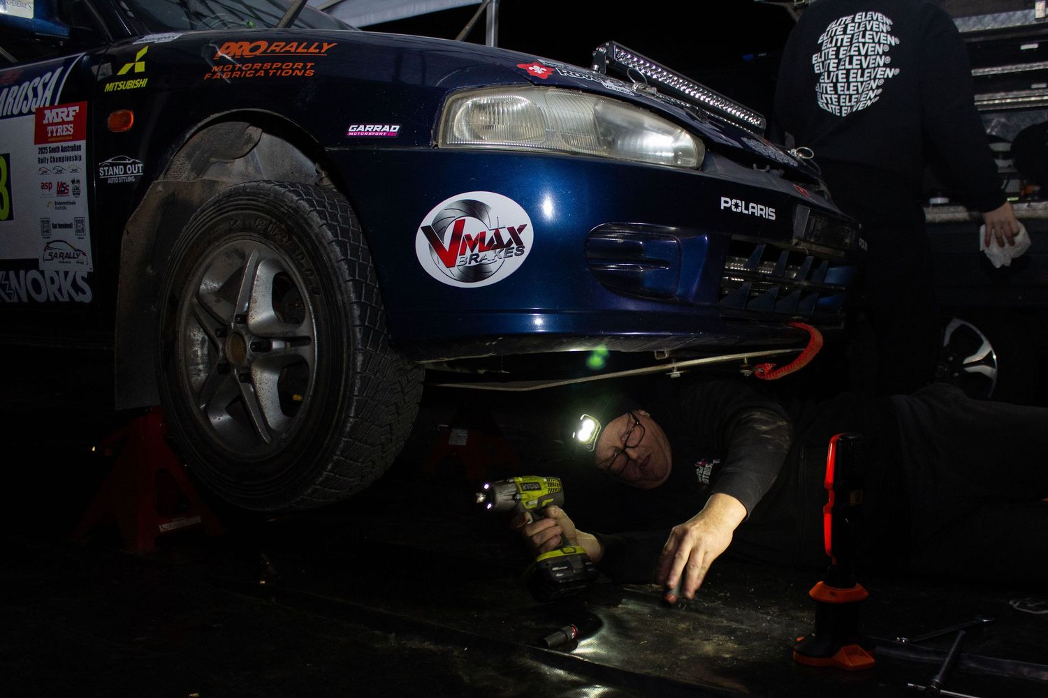 Dark racing car being worked on in low light conditions with tools visible.