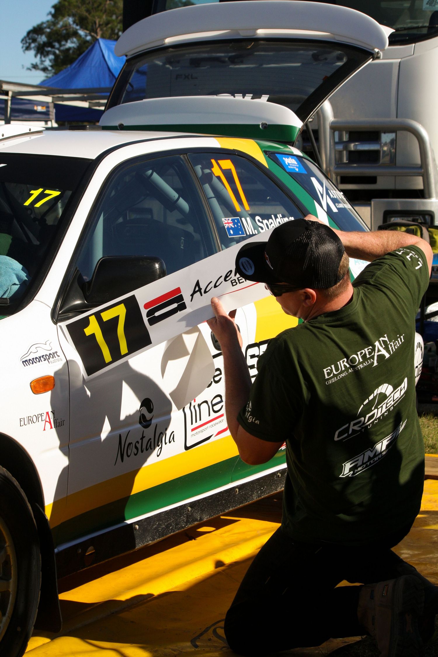 Crew member inspects race car number 17 in the paddock area.
