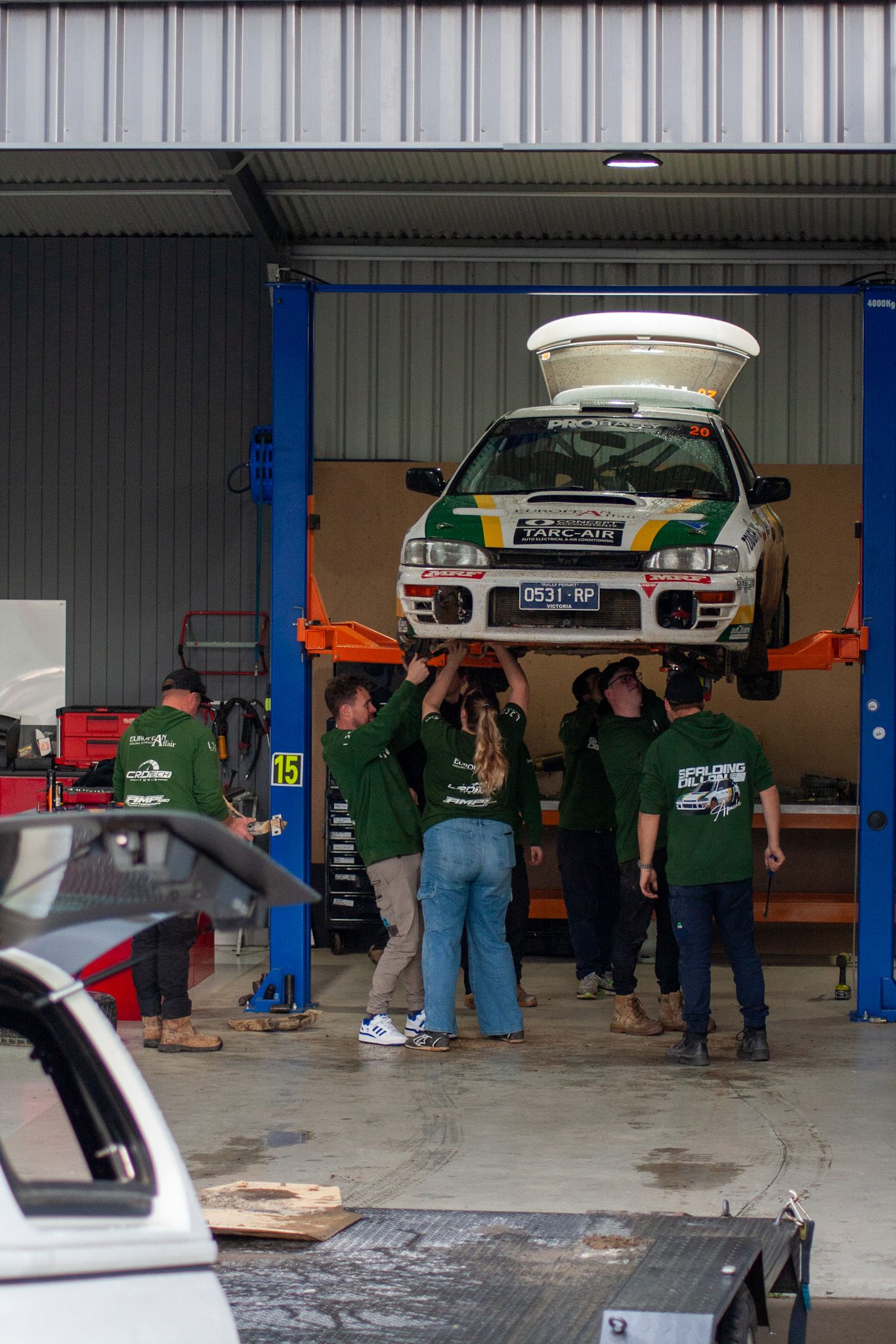 Mechanics working on raised race cars inside a professional garage facility.