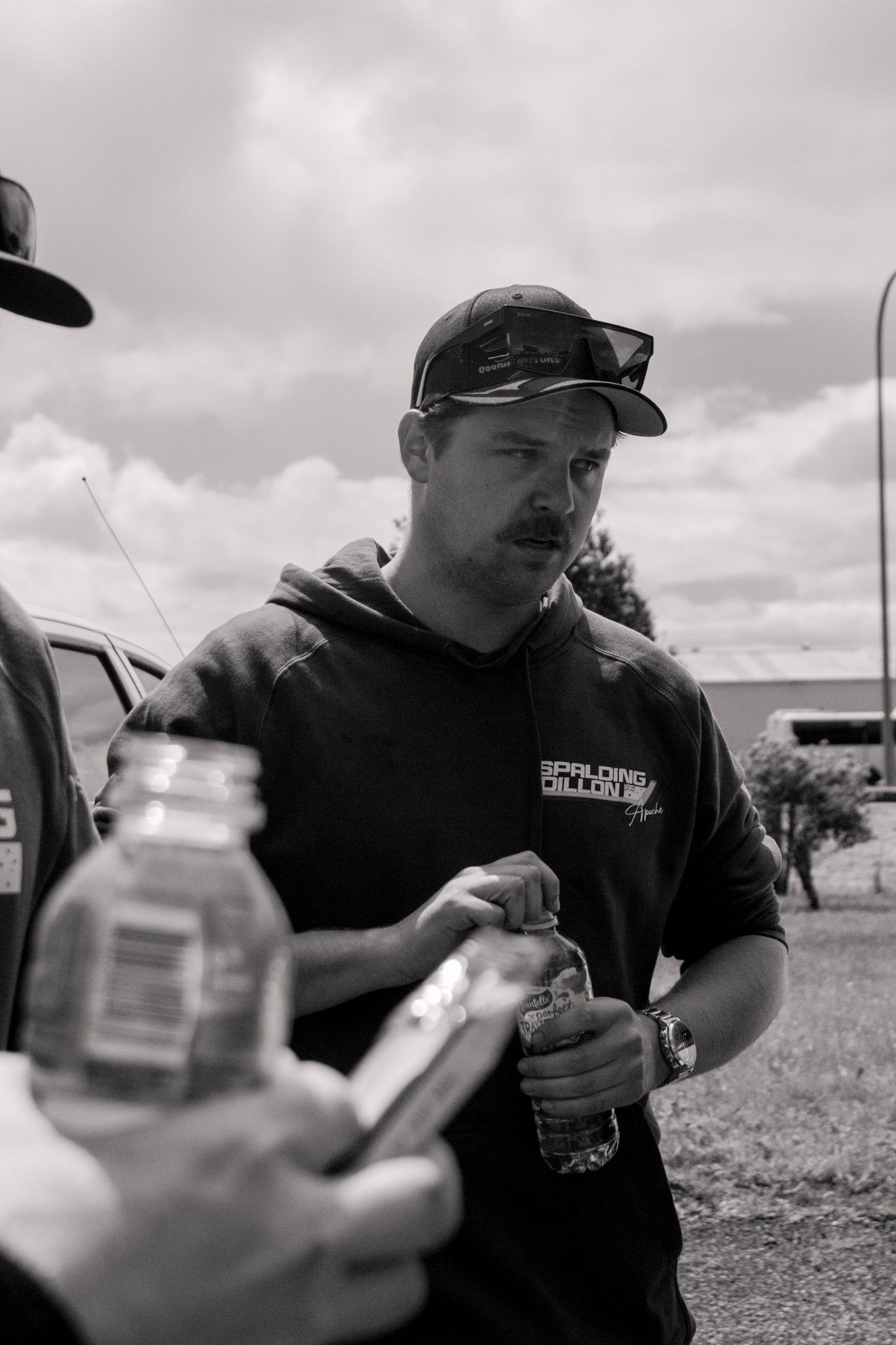 Racing team member in black uniform examines equipment at outdoor event.
