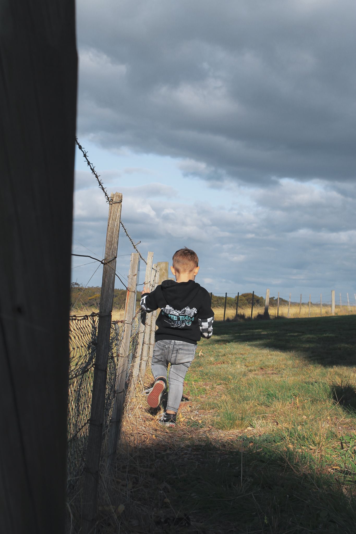 A silhouette walks along a fenced path during golden hour in a rural setting.