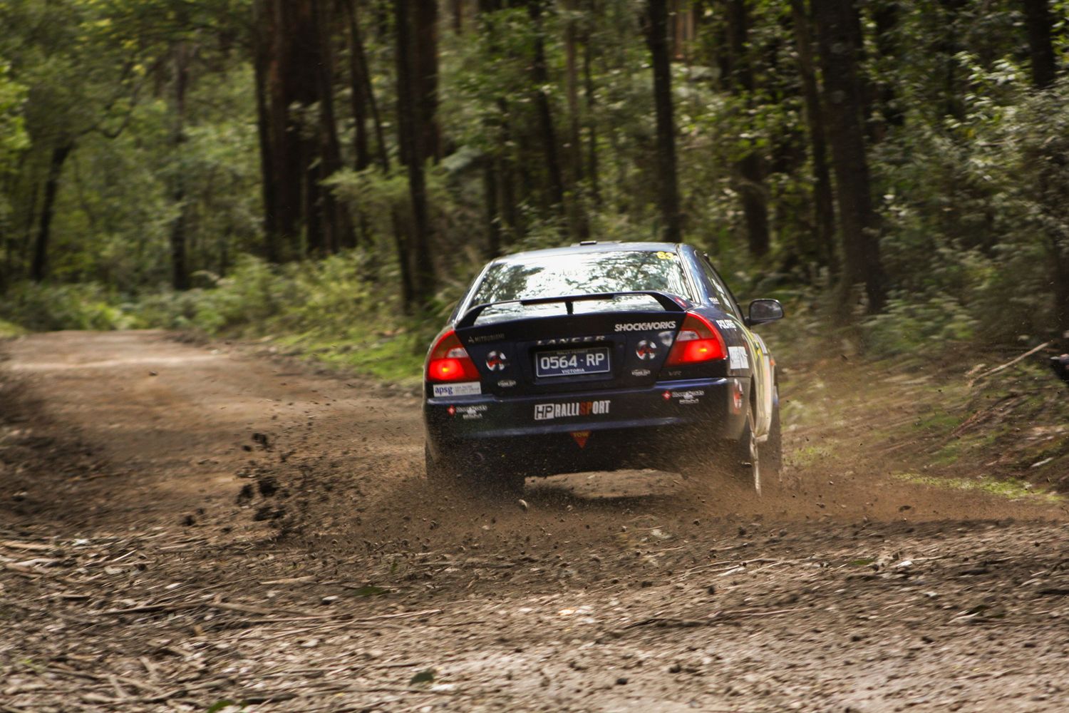 Rally car racing through dirt track in wooded forest area.