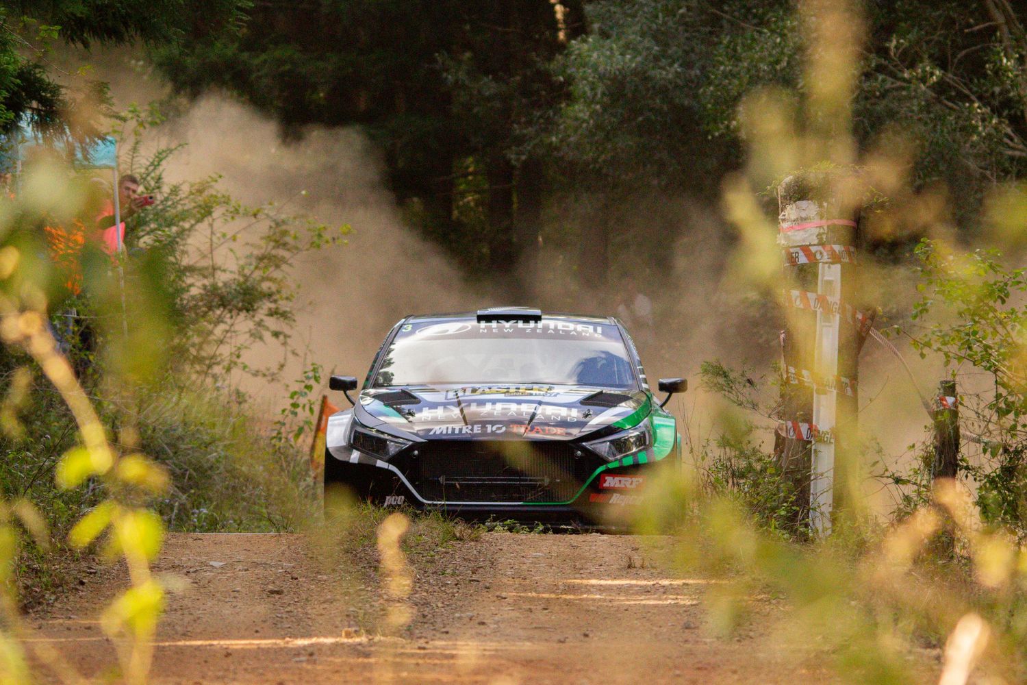 Rally cars racing through a dusty forest course during competition.