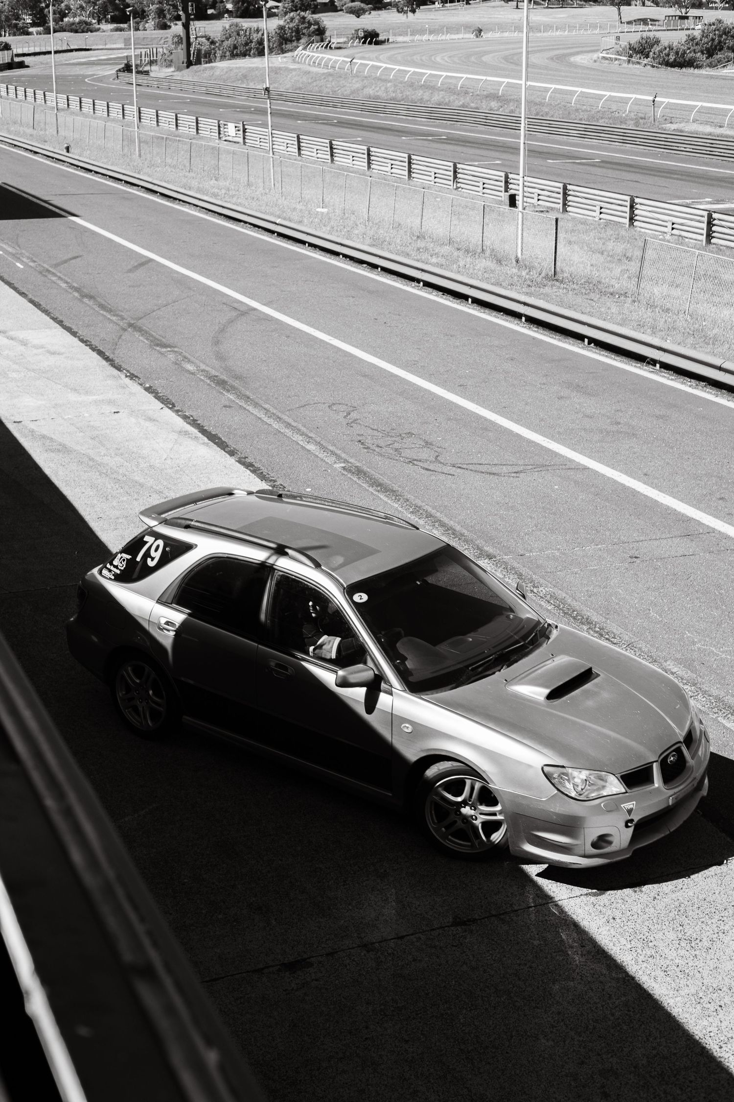 A modified Subaru WRX STI parked on a road with metal barriers in black and white photography.