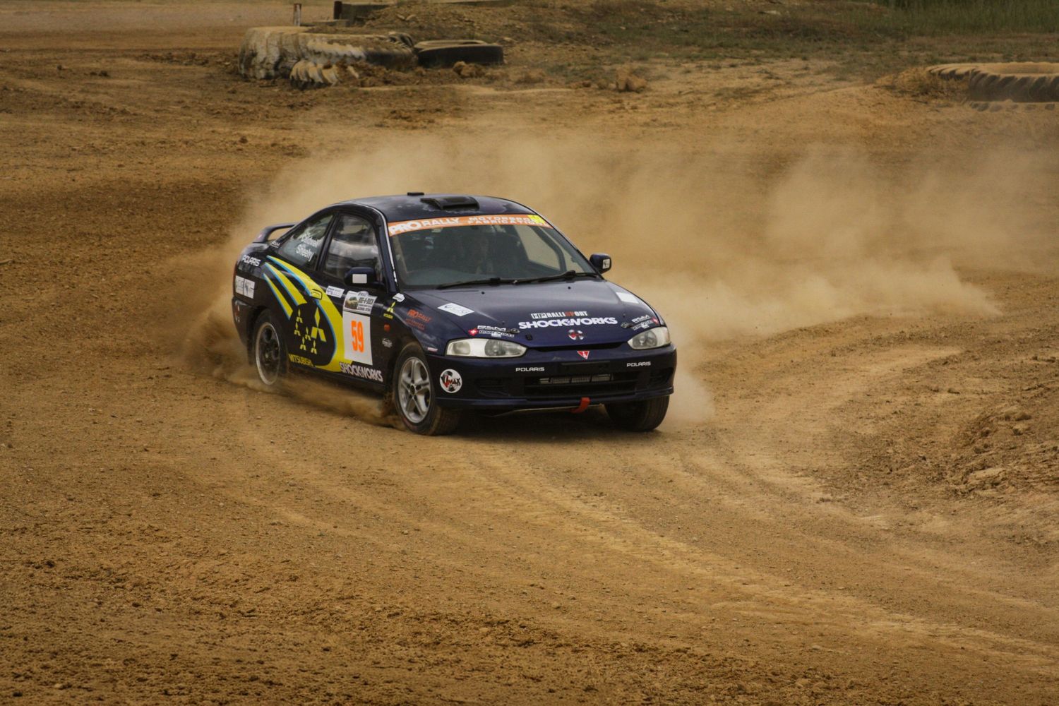 Subaru Impreza rally car powersliding through dusty corner.