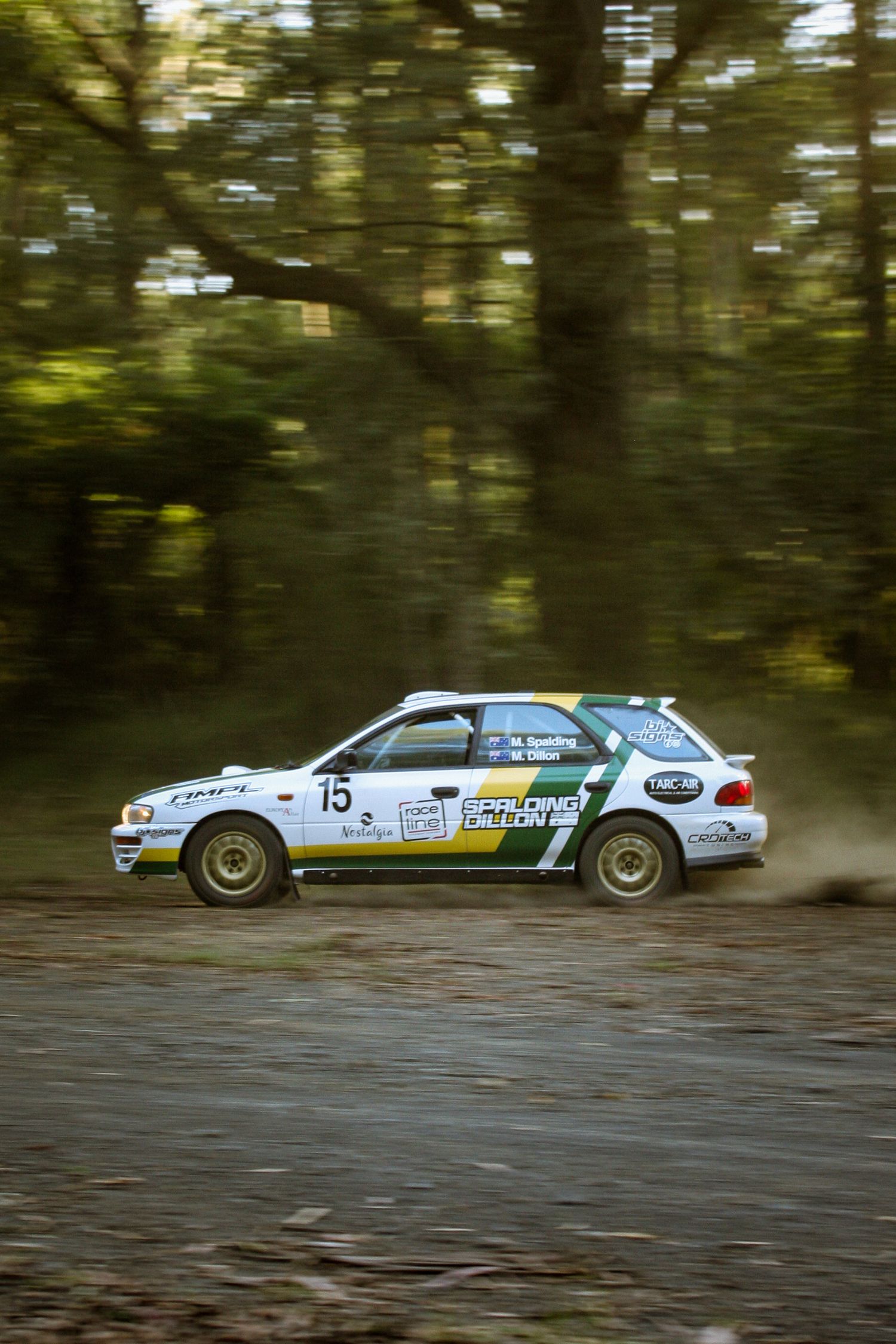 Motion blur shot of white rally cars racing through a wooded course.