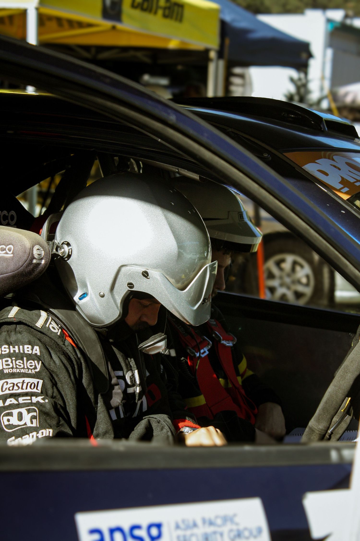 Helmeted drivers seated in race cars at a motorsport event.