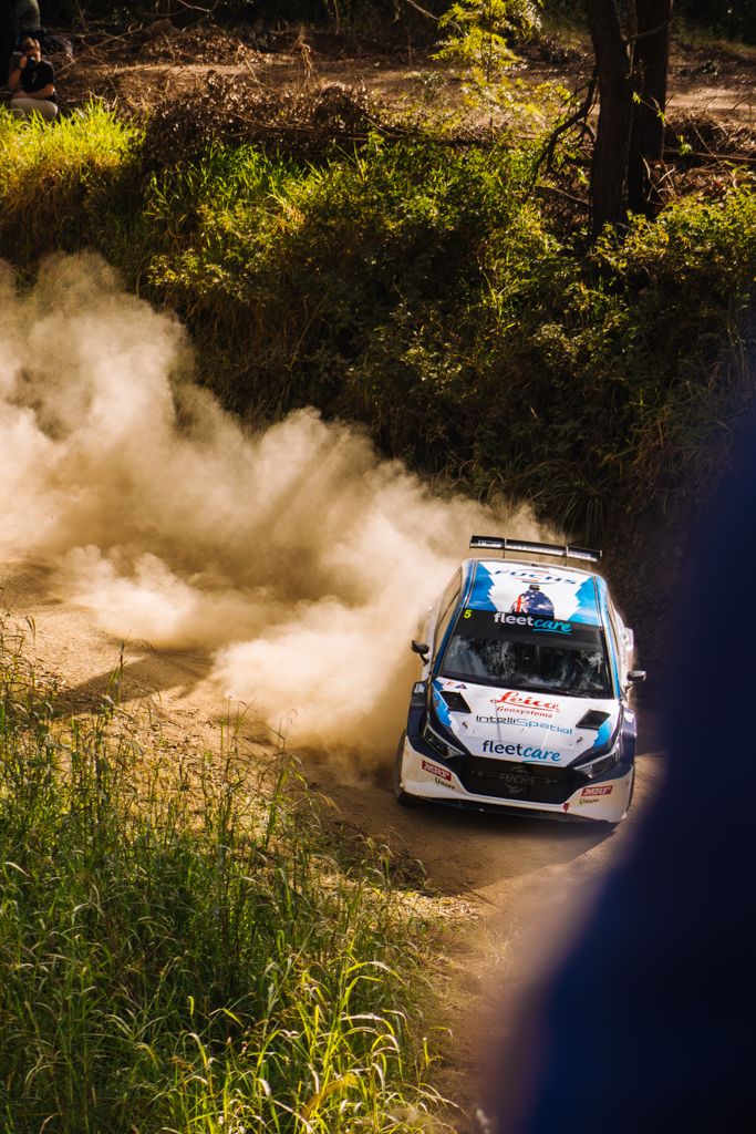 Rally car kicking up dust while racing through a grassy course on a sunny day.