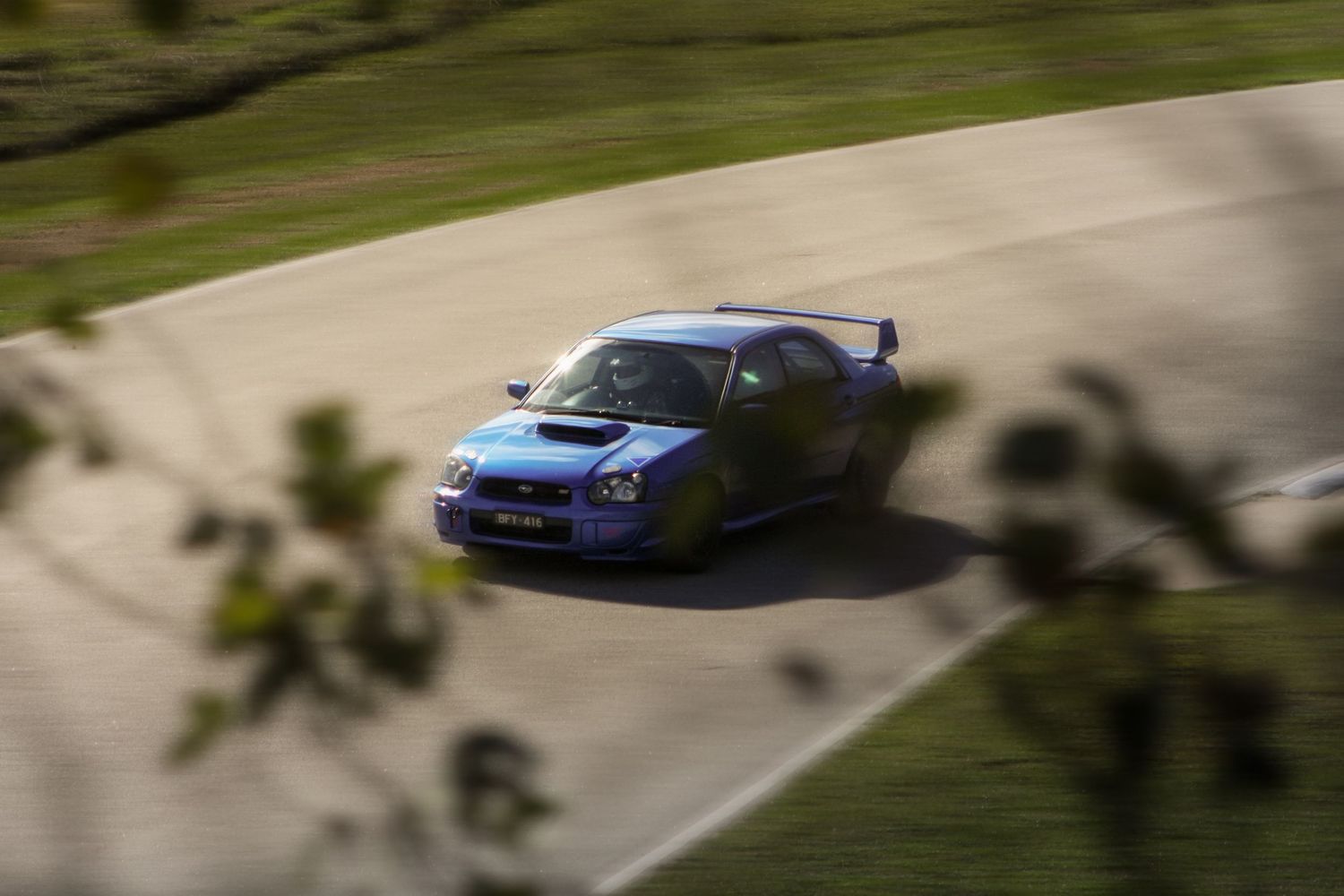 Blue Subaru WRX STI rally car races through curved dirt track section.