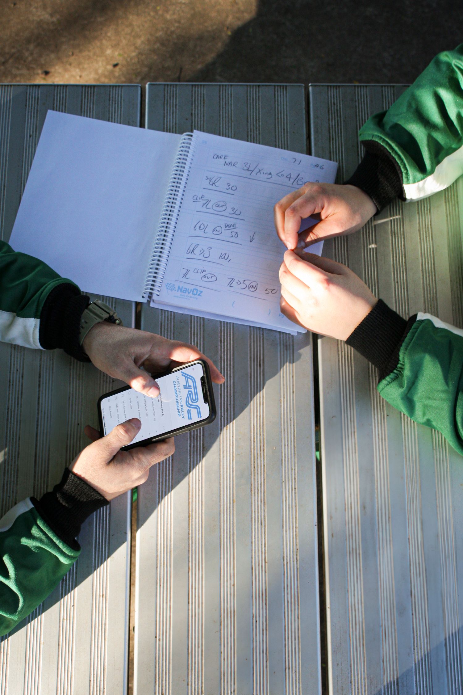 Hands holding a phone and notebook with calculations on a wooden surface.
