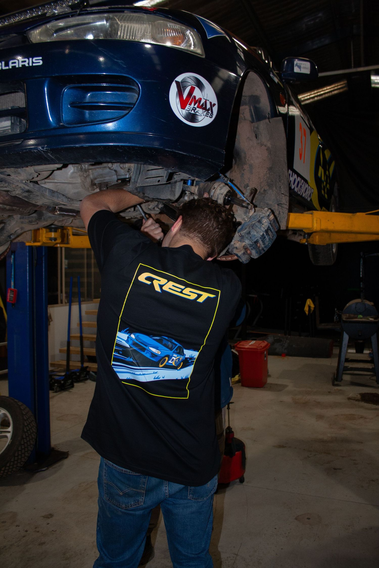 Mechanic working underneath a lifted blue car in a garage workshop.