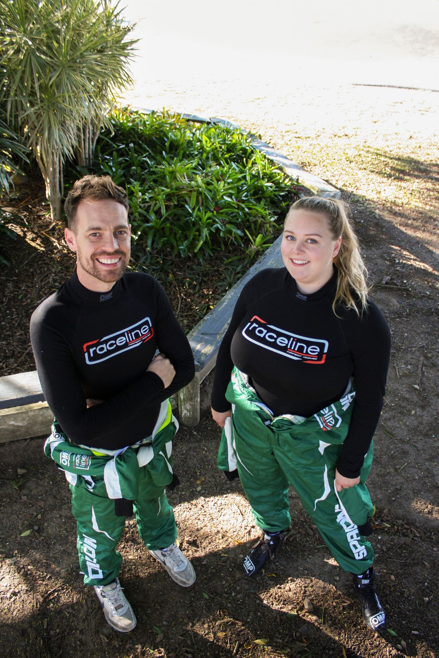 Two team members wearing matching black racing crew uniforms standing outdoors.