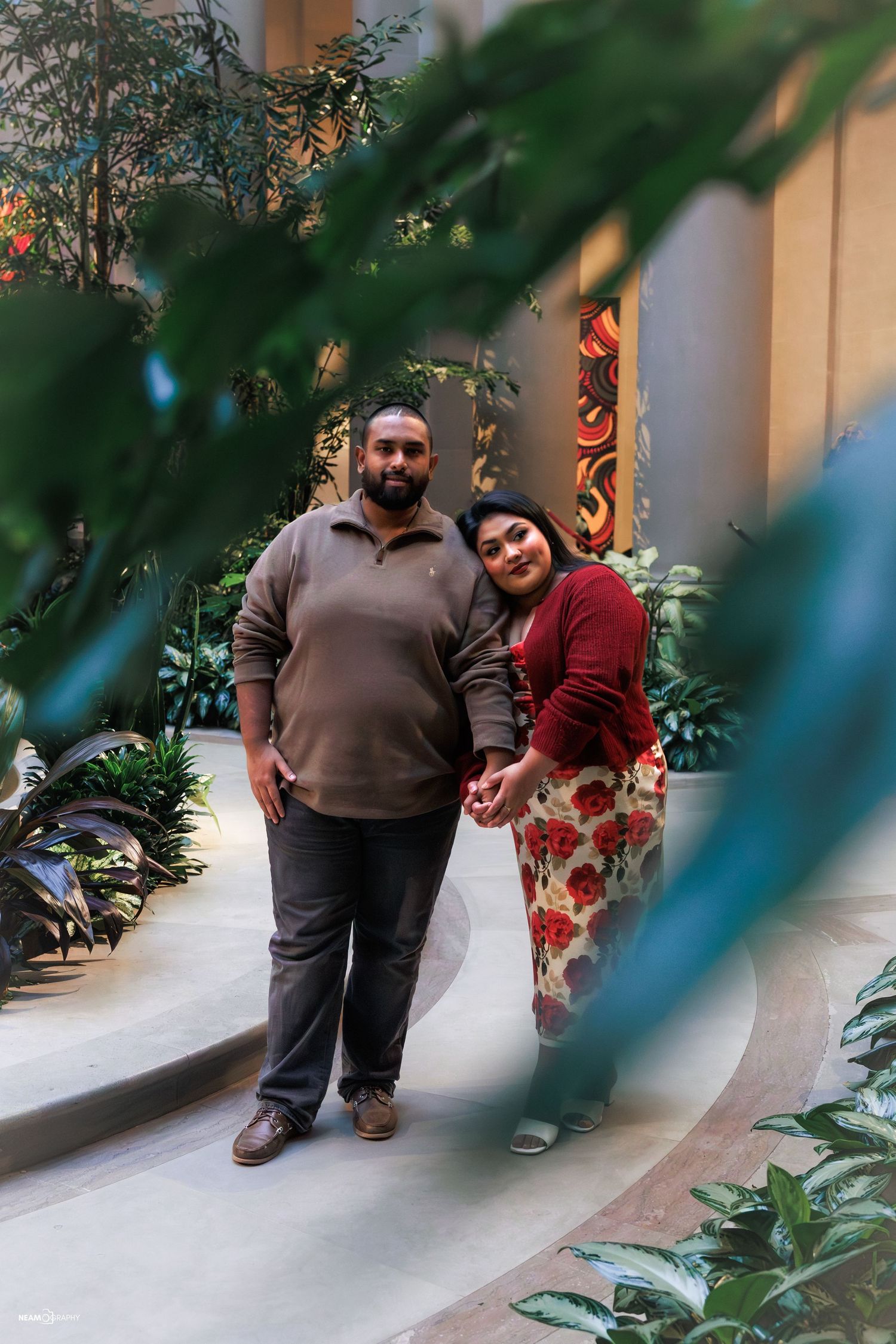 Artistic South Asian engagement session at National Gallery of Art DC, couple framed by greenery with woman resting head on man's shoulder.