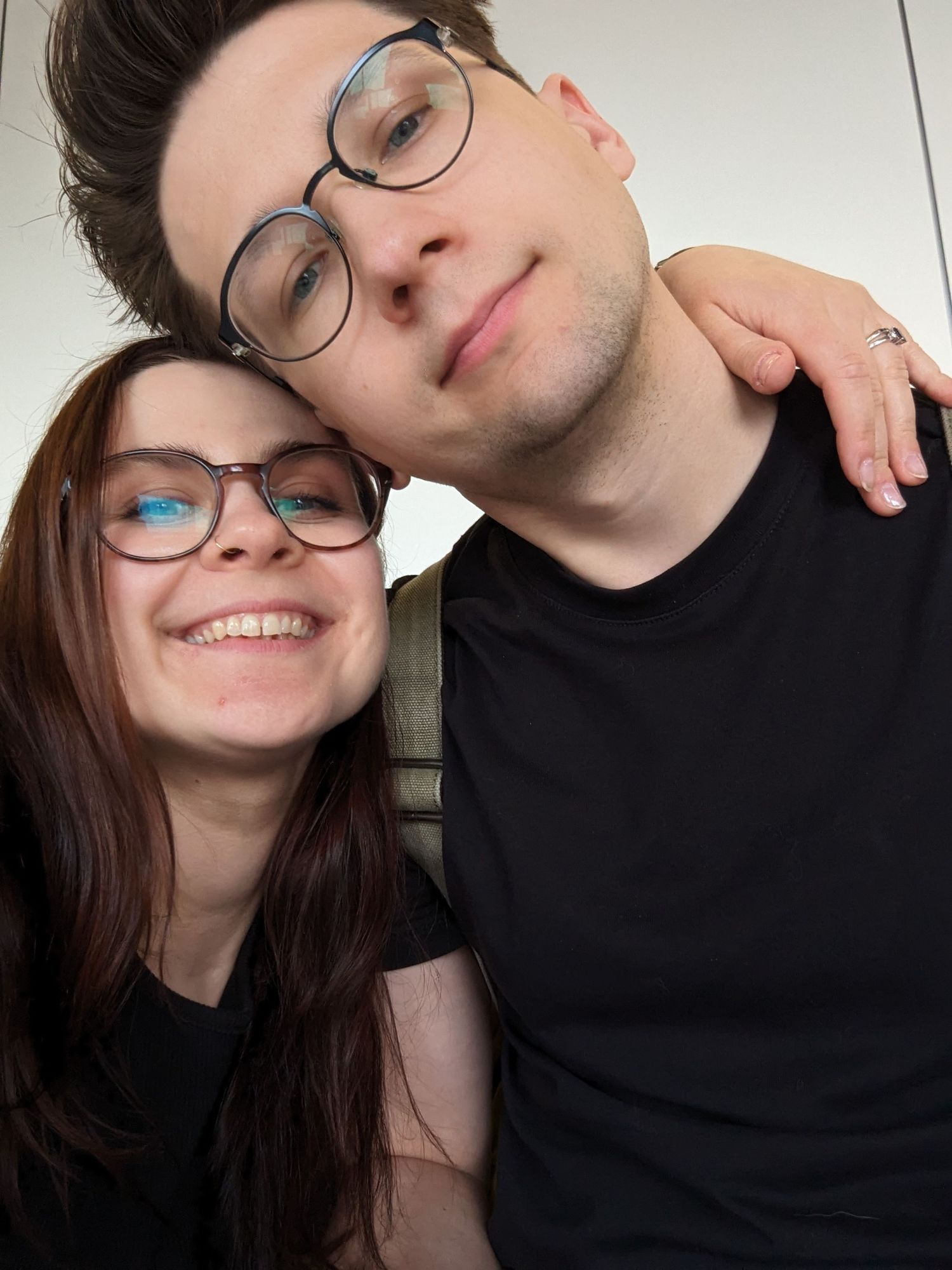 A smiling couple wearing matching round glasses pose for a close-up selfie together.