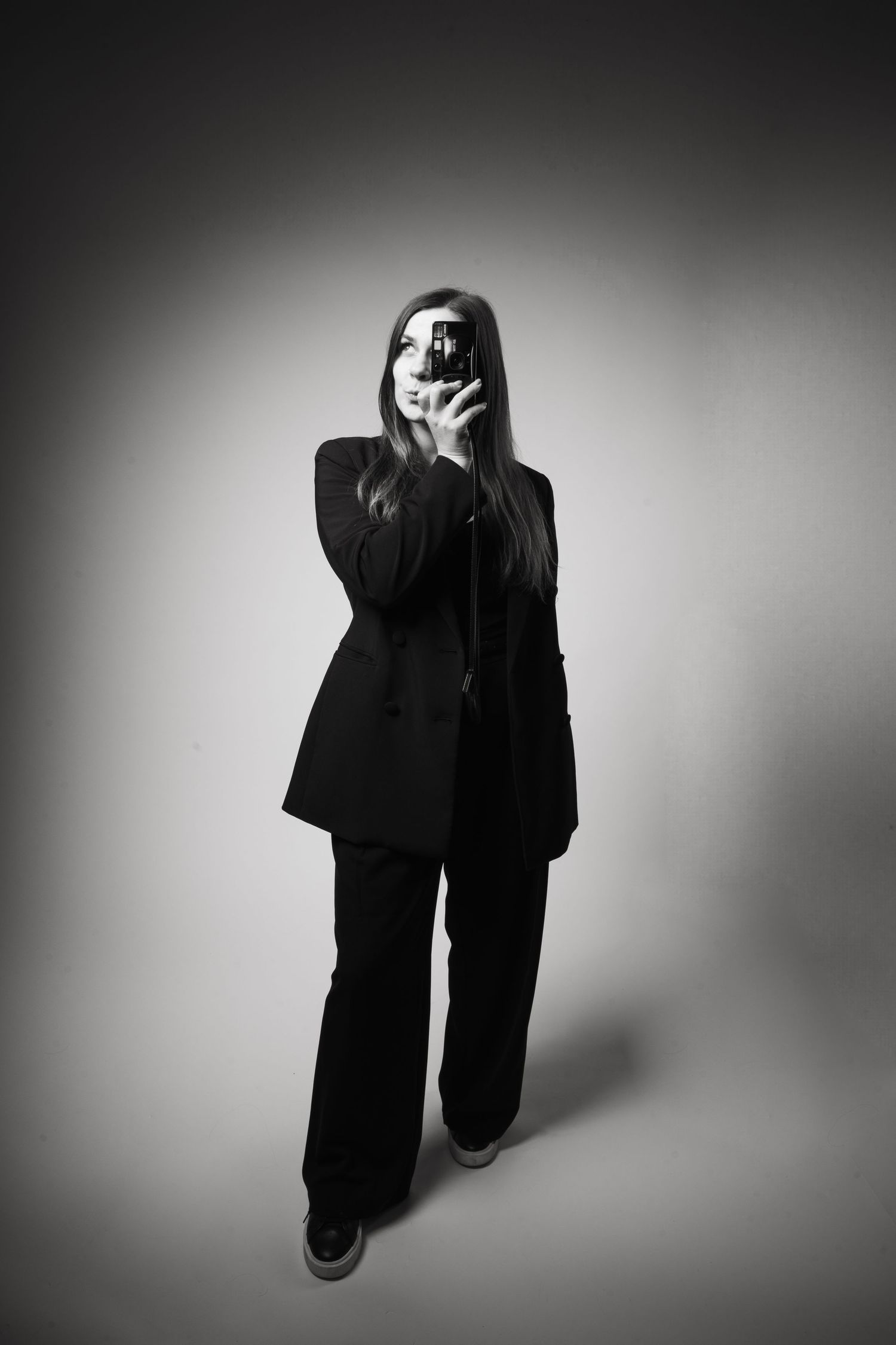 A moody black and white photo of a person in a dark business suit standing against a gradient background.