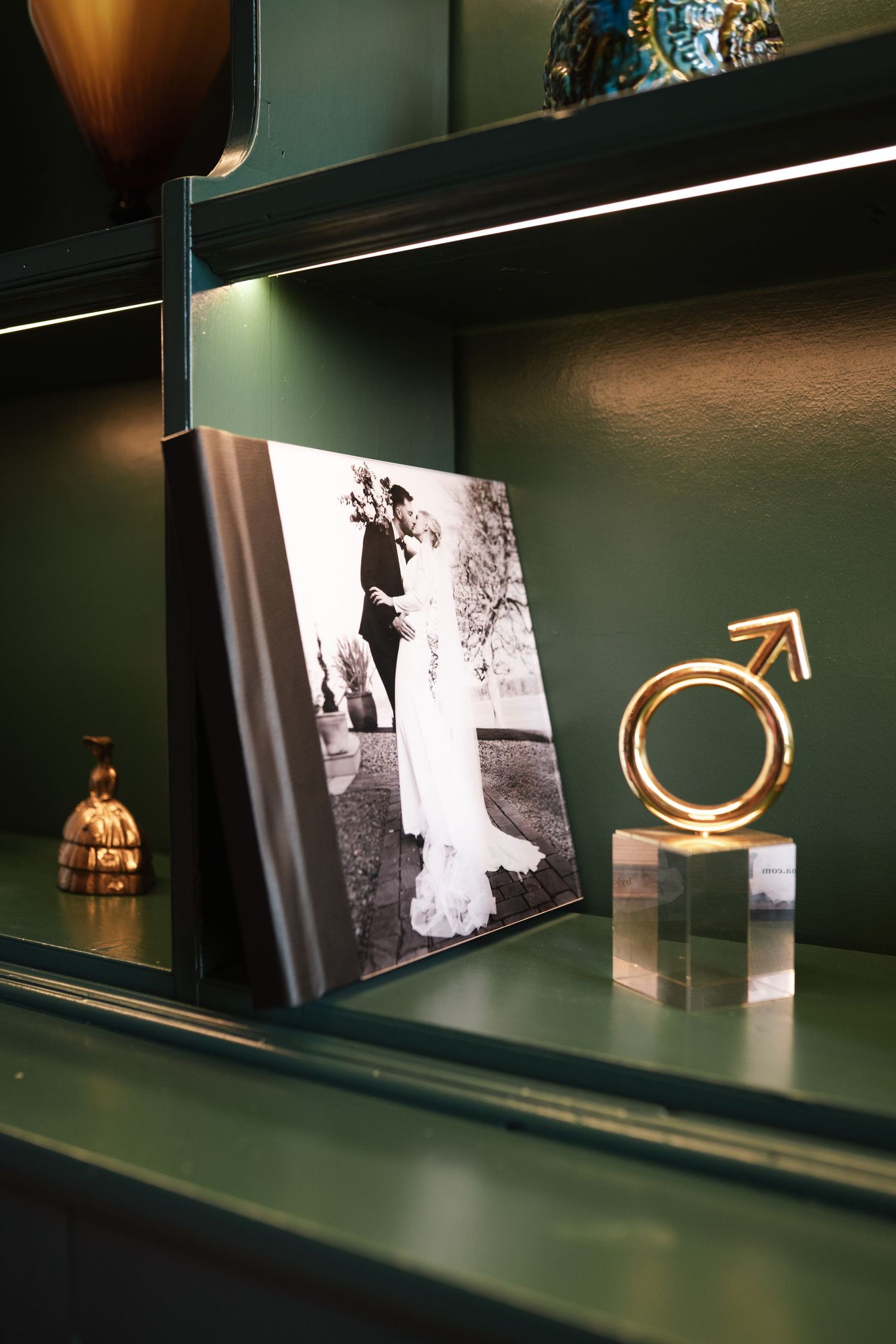 Decorative shelf display with black and white wedding photo and gold male gender symbol on dark green background.
