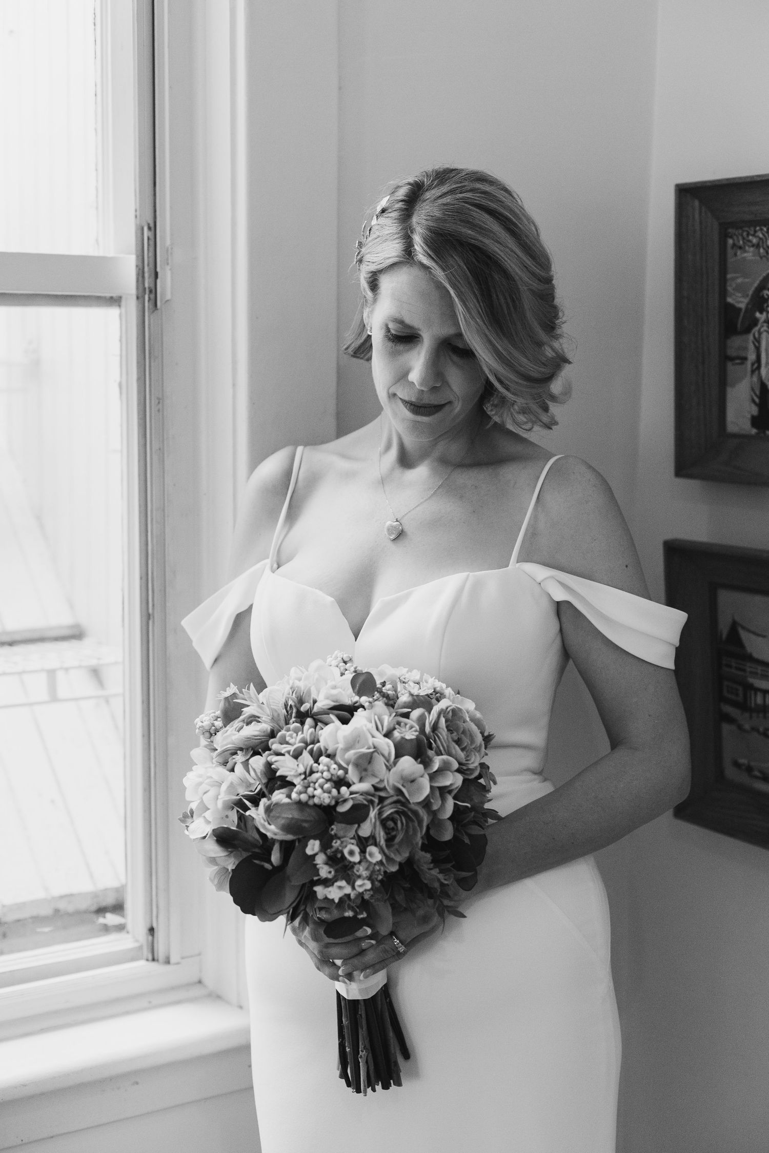 beautiful bride standing by a window looking down at her bouquet of flowers