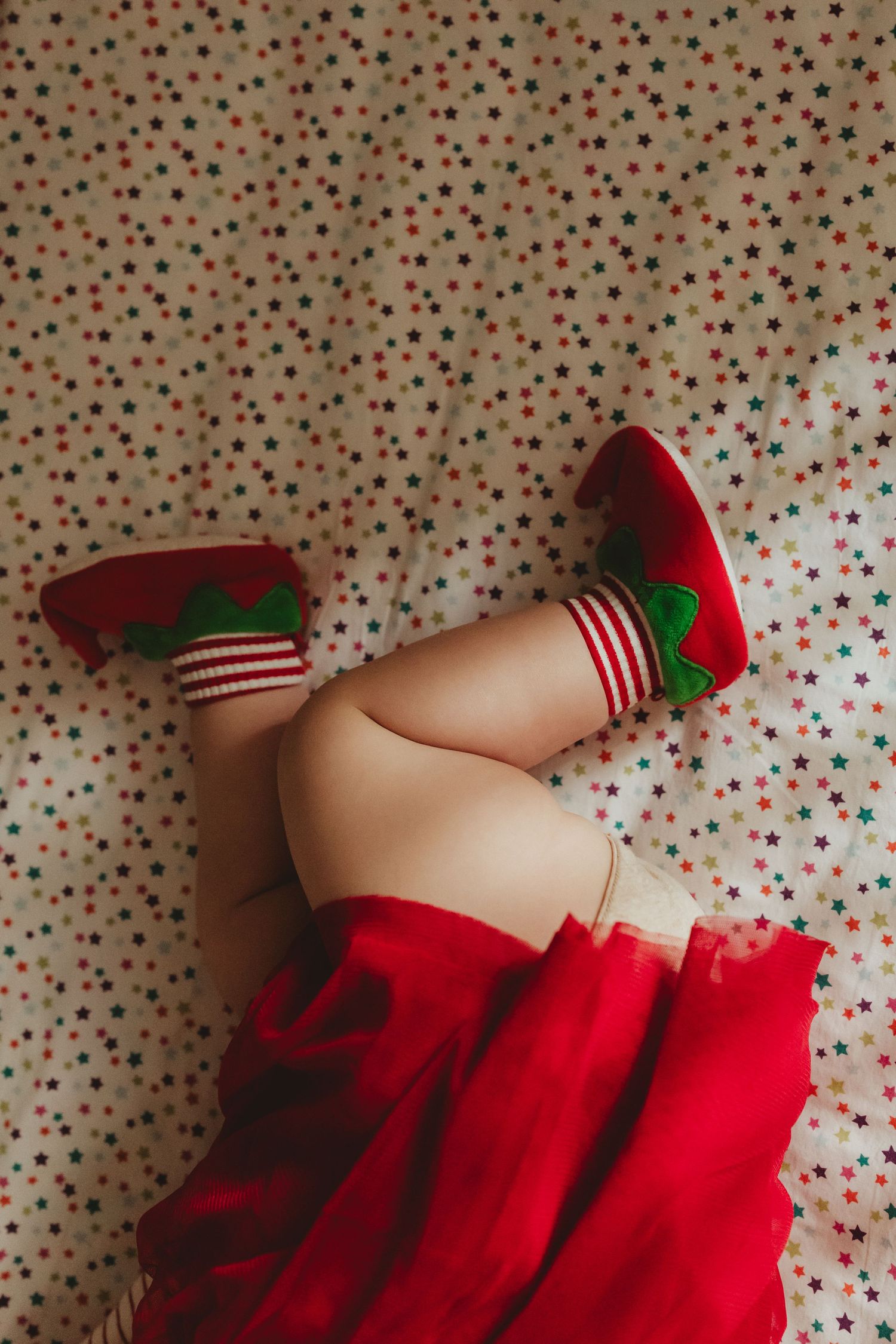 Striped red and white elf socks peeking out from red ruffled fabric against a polka dot background.