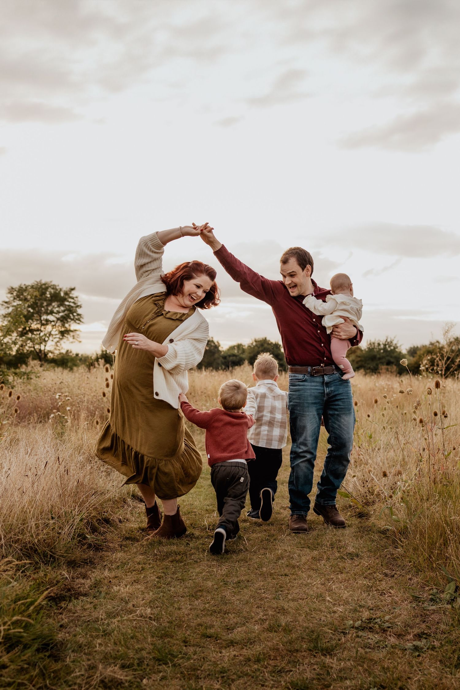 A family dances together joyfully in a golden autumn field at sunset.