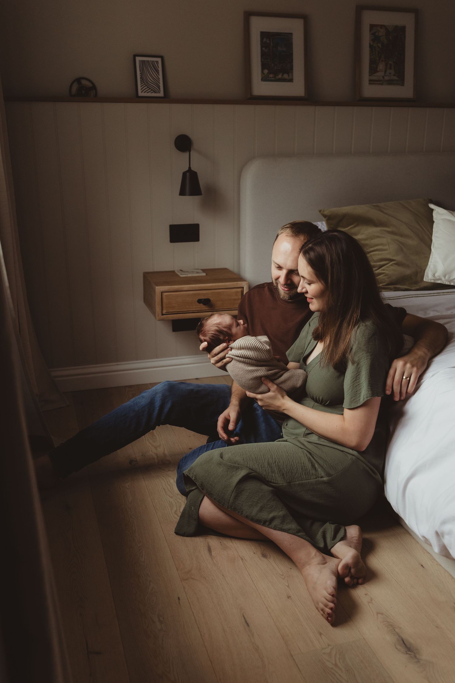 Person in green shirt lying on wooden floor while using mobile phone in dimly lit room.