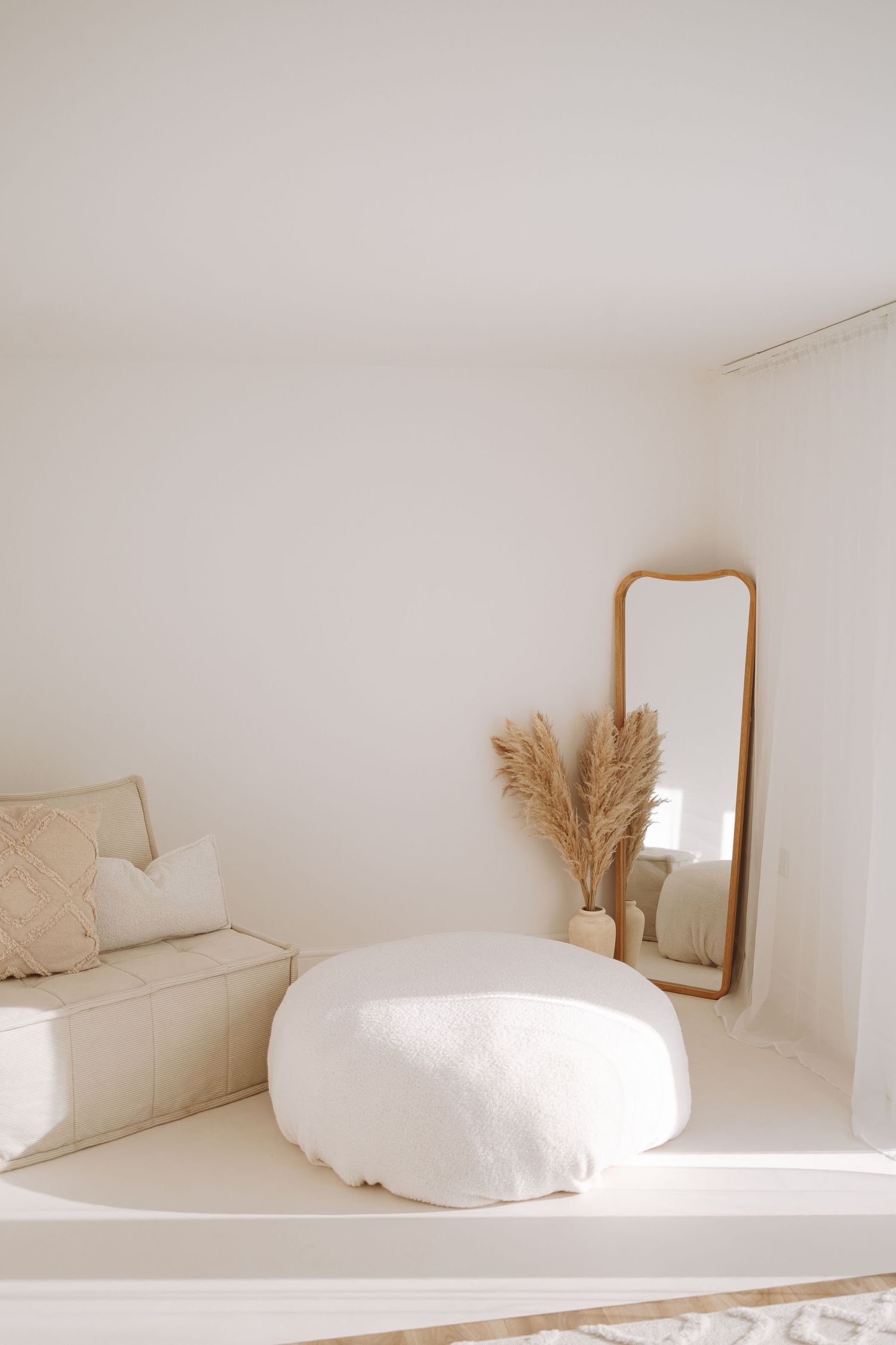 A minimalist white room interior with wooden mirror frames and decorative dried pampas grass against light walls.
