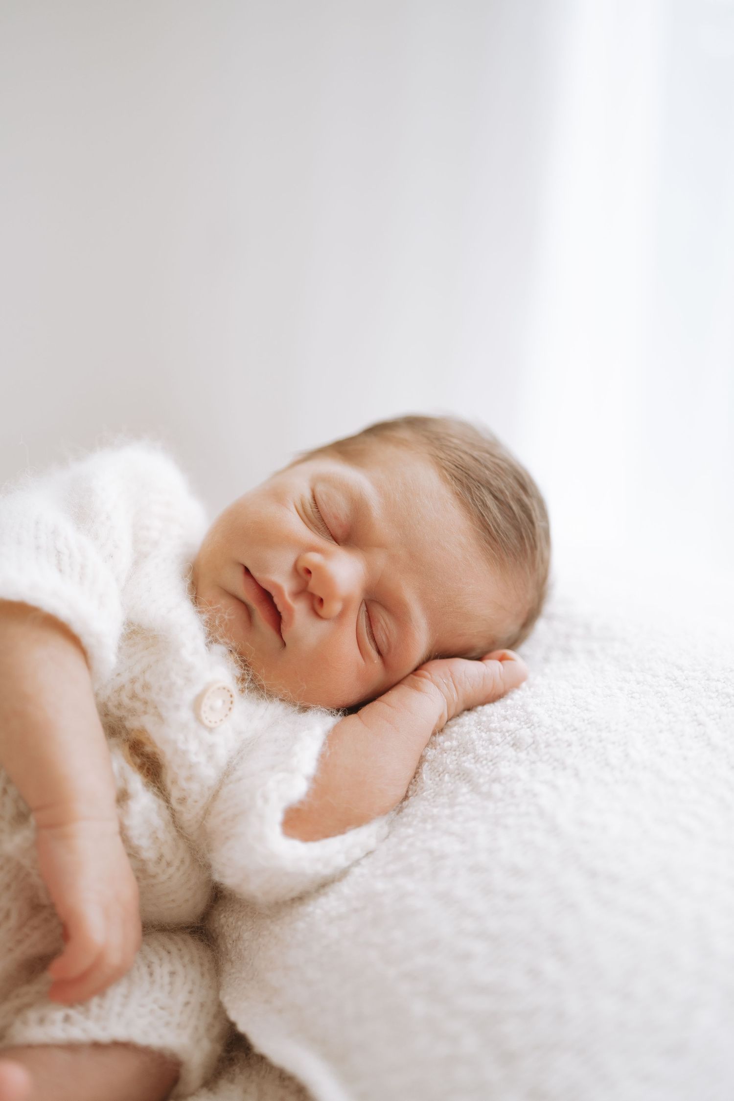 Newborn baby sleeping peacefully on soft white blanket in serene lighting.