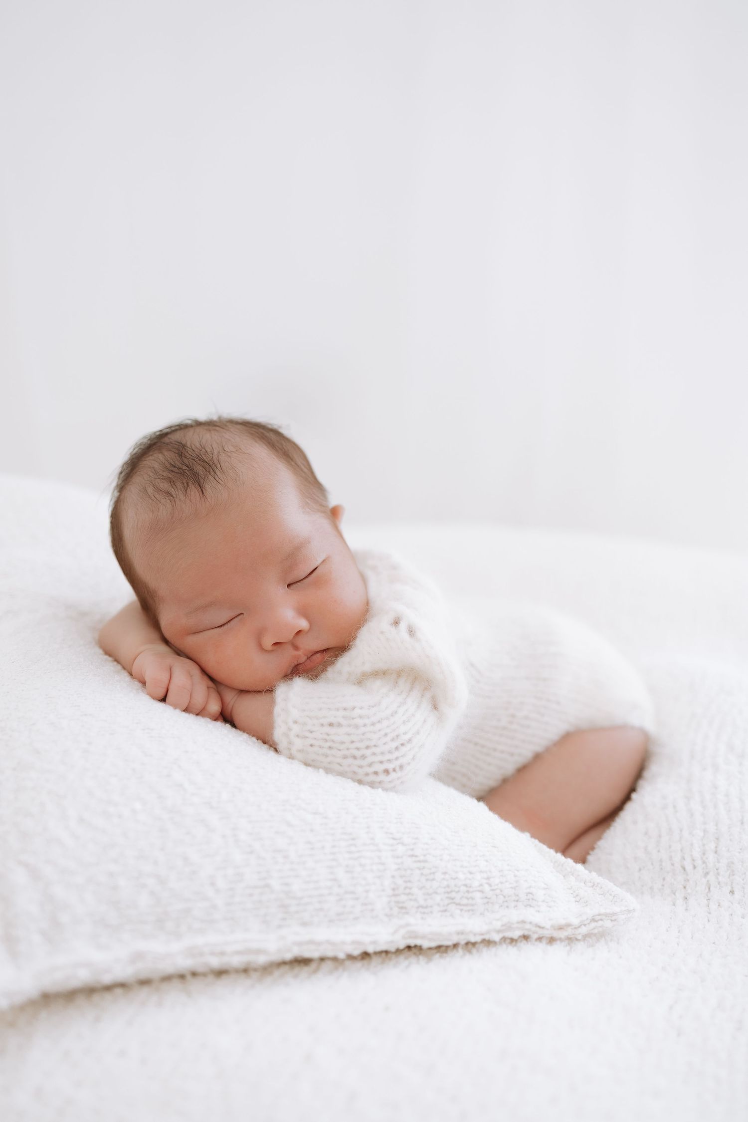 A peaceful sleeping newborn wrapped in soft white blankets on a white background.