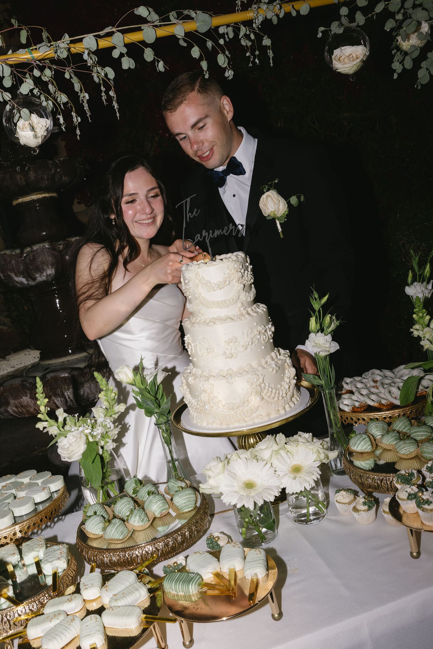 A wedding reception dessert table features an elegant white tiered cake and cupcakes arranged on ornate gold stands.