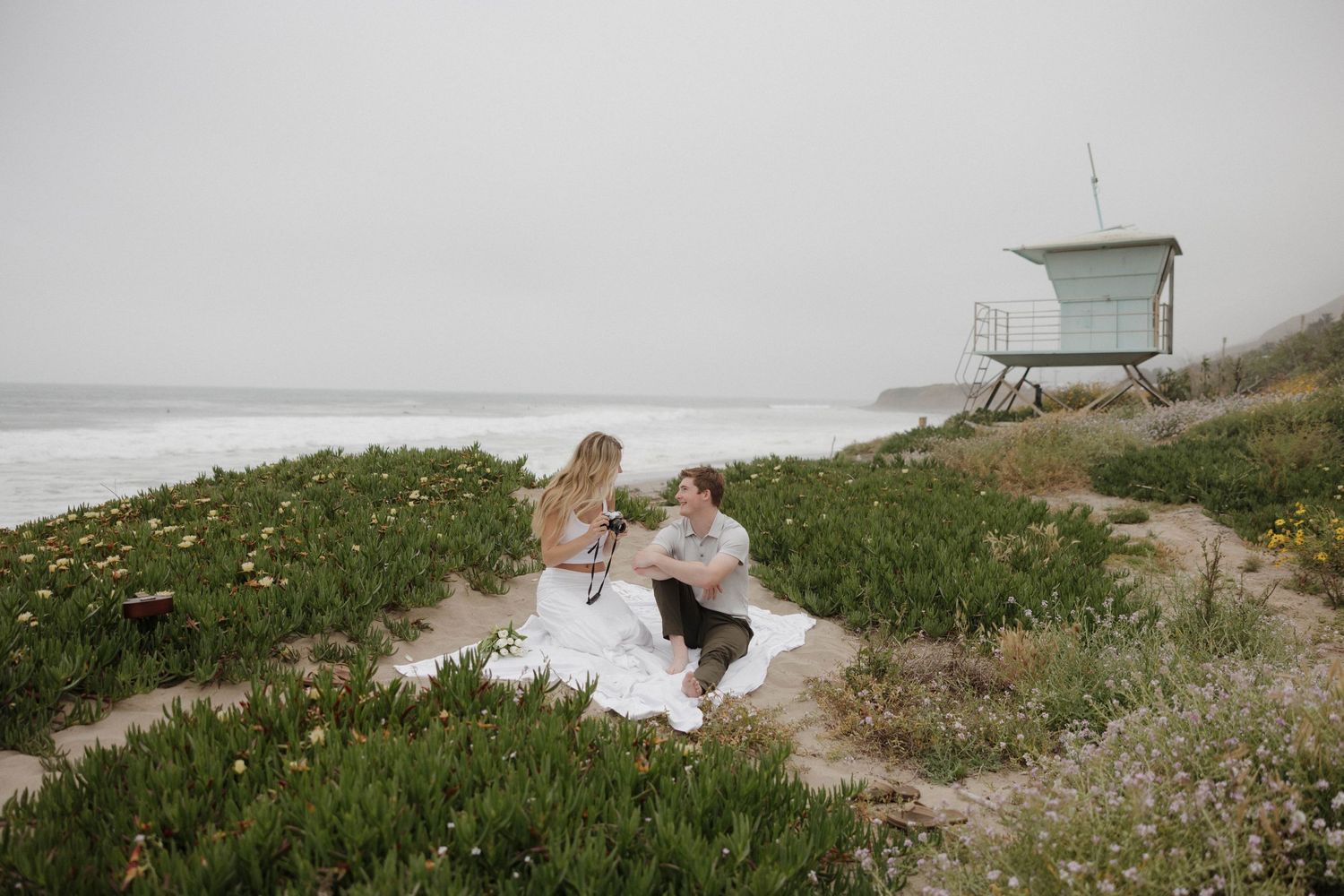 A picnic scene on a grassy hill overlooking the ocean with a lifeguard tower in the background.
