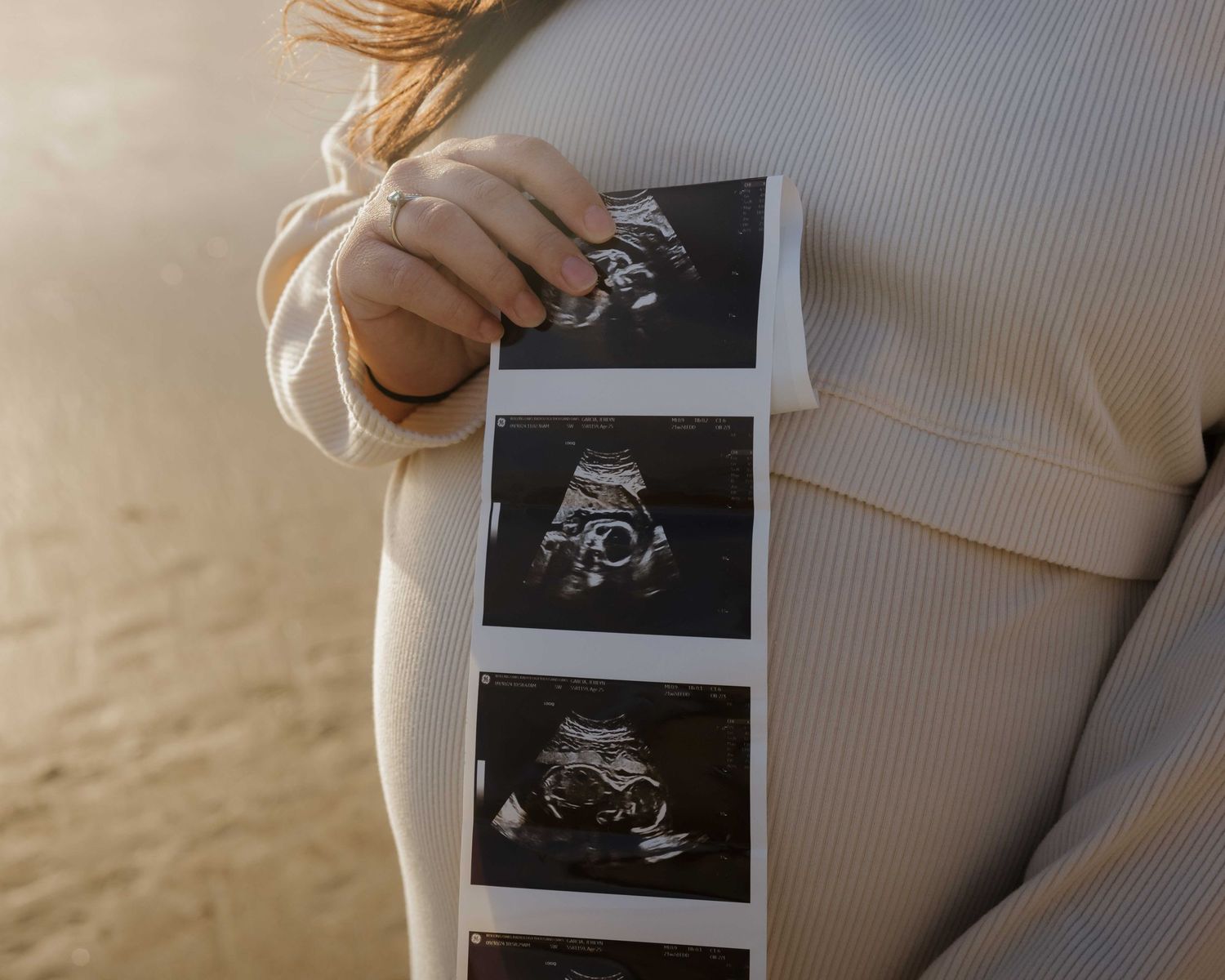 A strip of three black and white ultrasound images being held against someone wearing a soft white sweater.