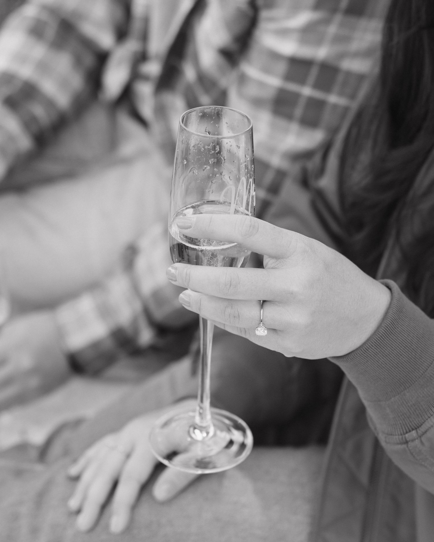 A hand holds a champagne flute with a light-colored beverage in black and white photography.