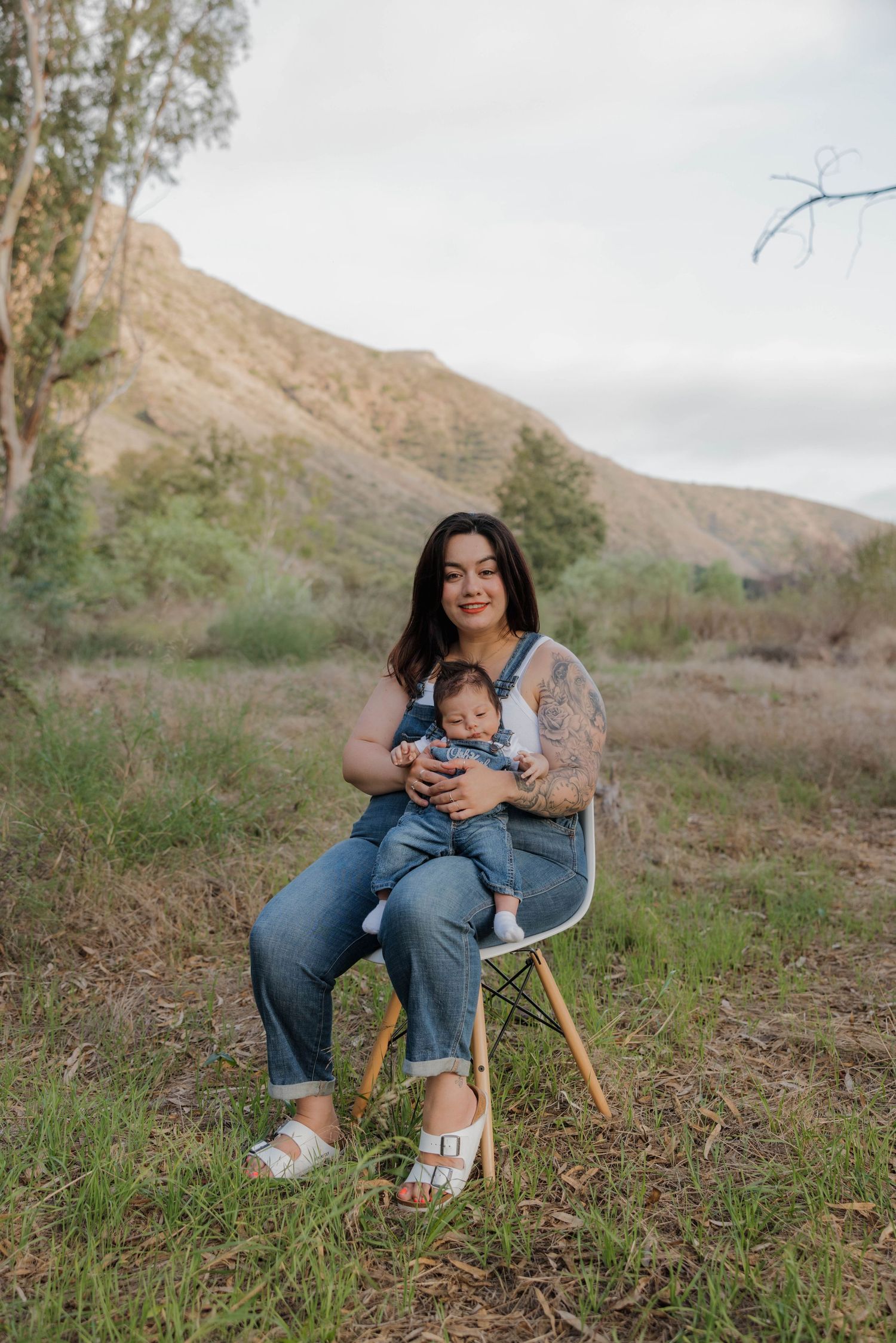 Parent and child sitting together on a modern chair in an outdoor setting with mountains and trees in the background.