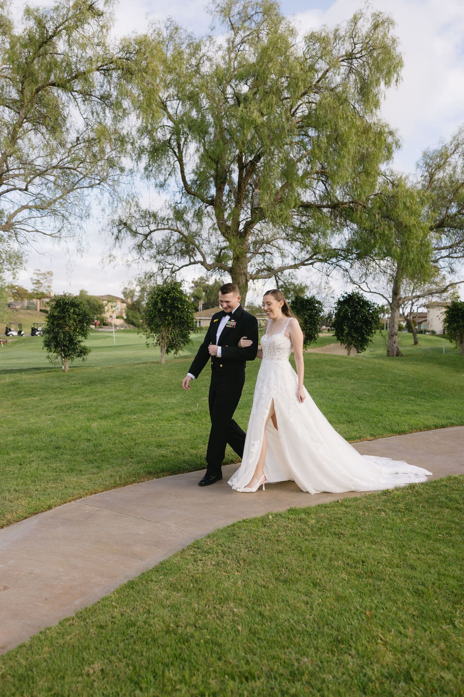 Bride and groom walking hand in hand on a curved path through lush green grounds on their wedding day.