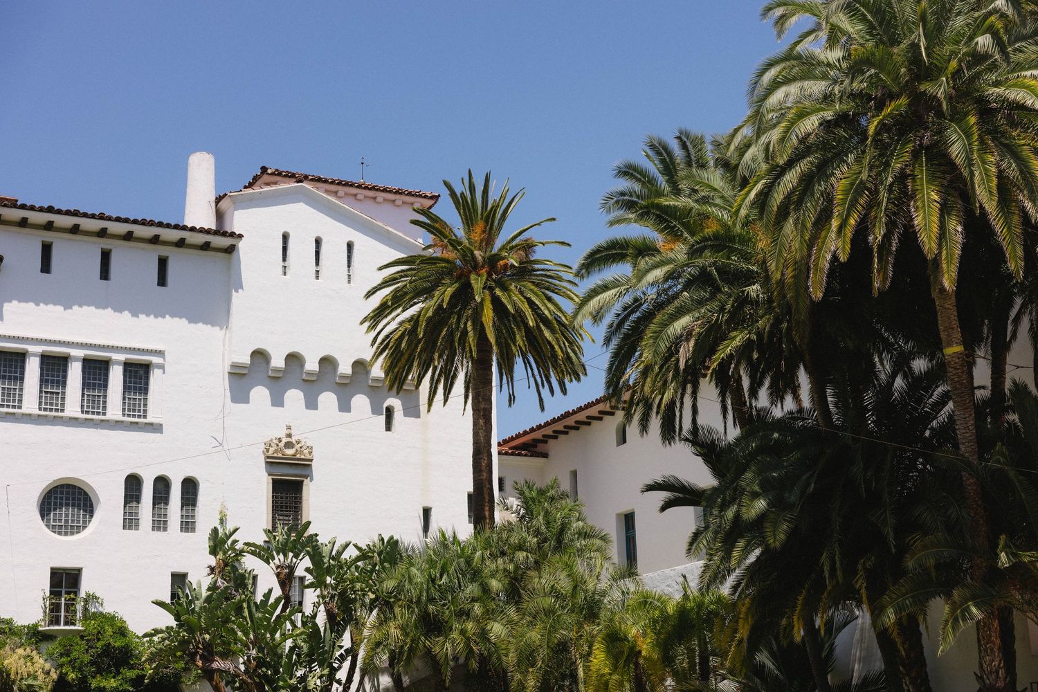White Spanish colonial style building with palm trees against blue sky.