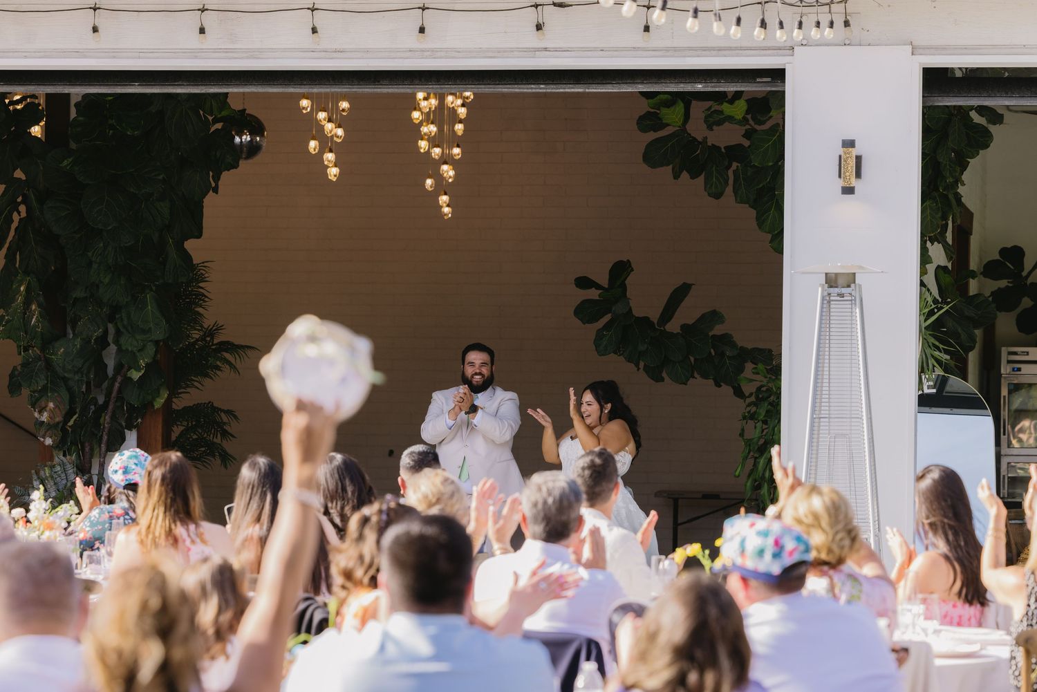 Couple sharing a toast with guests at an elegant outdoor wedding reception with string lights.
