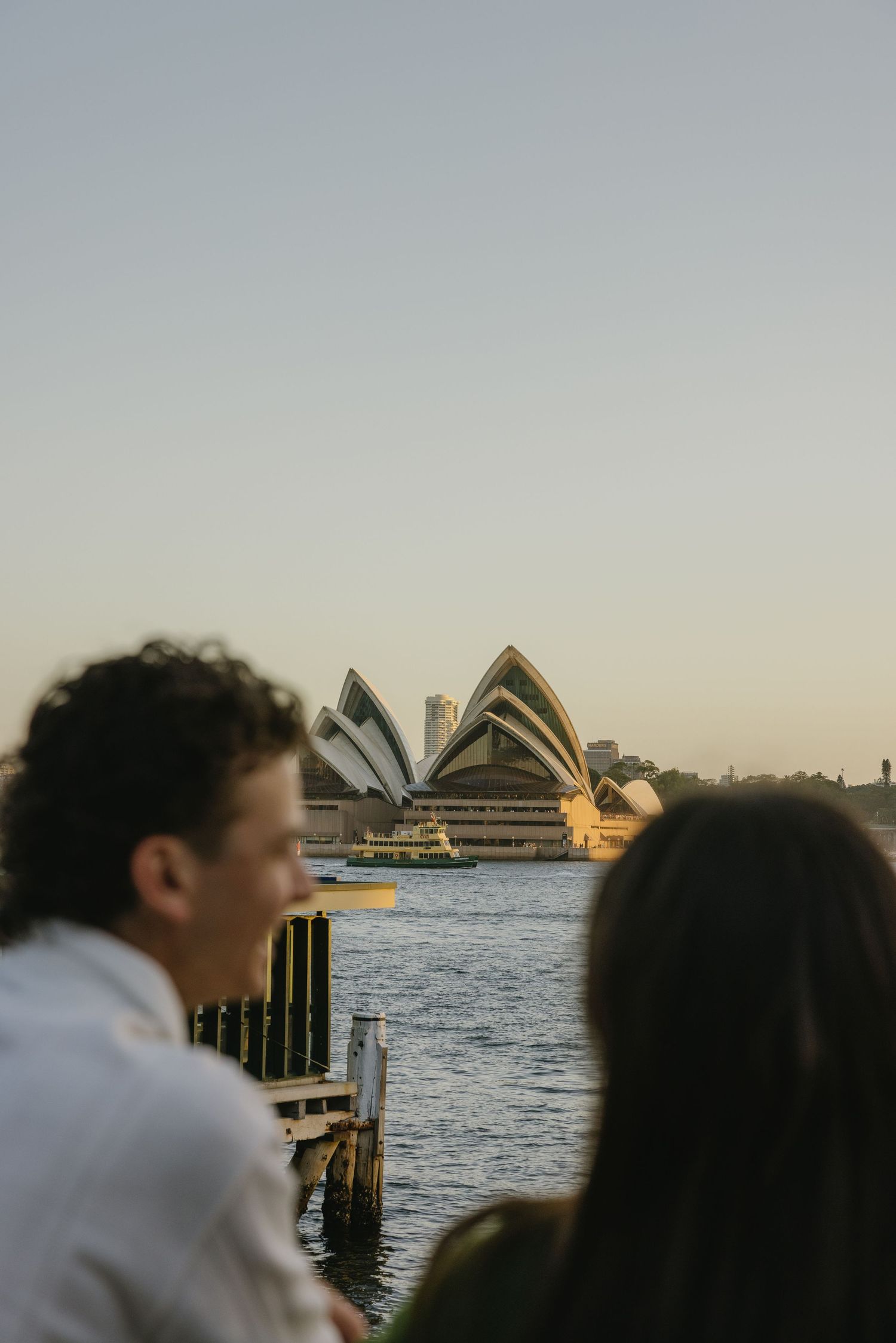 Couple admiring the iconic Sydney Opera House across the harbor at golden hour dusk in Australia.