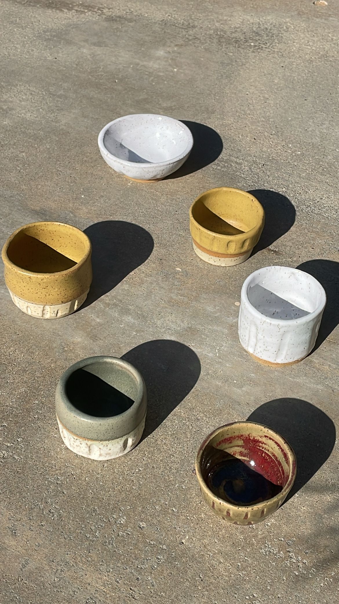 Various ceramic bowls in different colors cast shadows on concrete in bright sunlight.