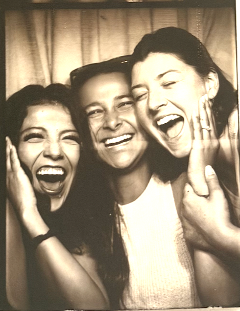 Three friends laughing joyfully together in a vintage sepia photo booth picture.