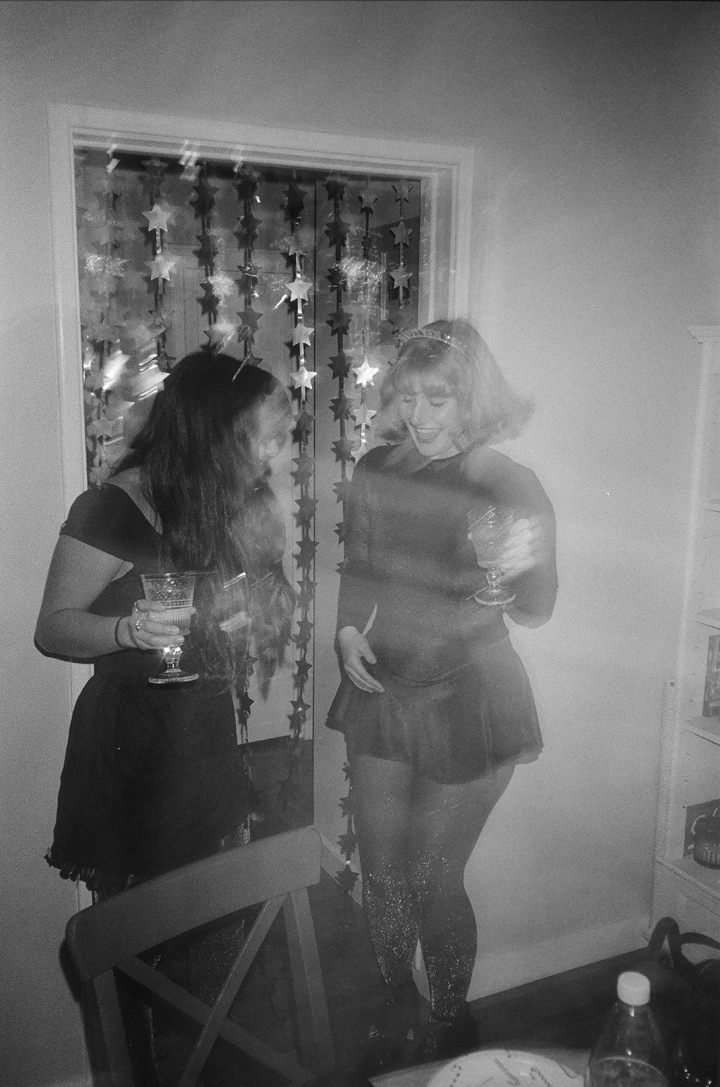 Two women in party attire holding drinks near a star-decorated doorway in a black and white photo.
