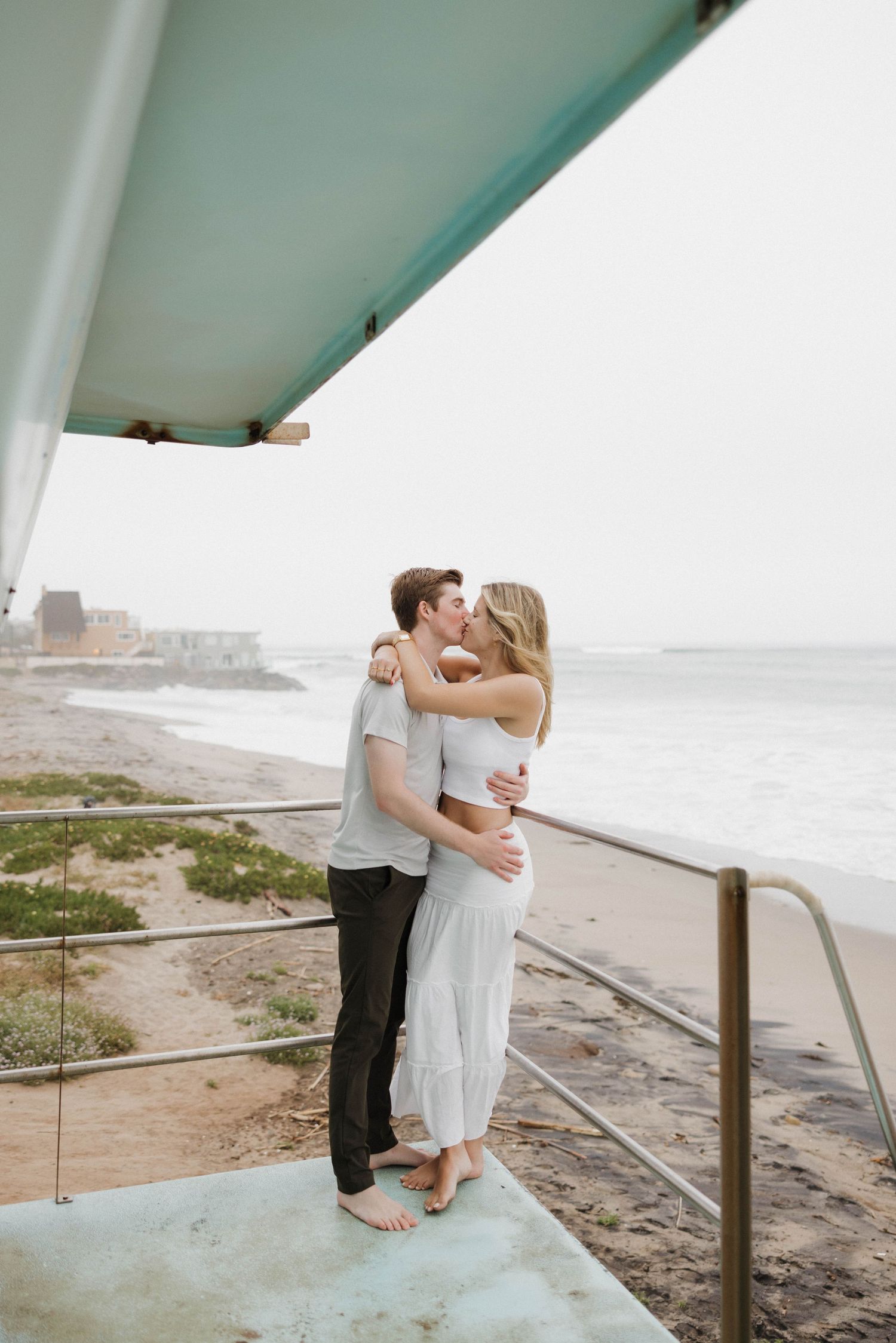 Couple embracing on a coastal viewpoint overlooking the ocean and beach.