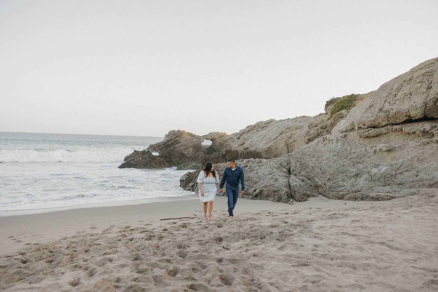 Couple walking along rocky coastline beach at sunset.