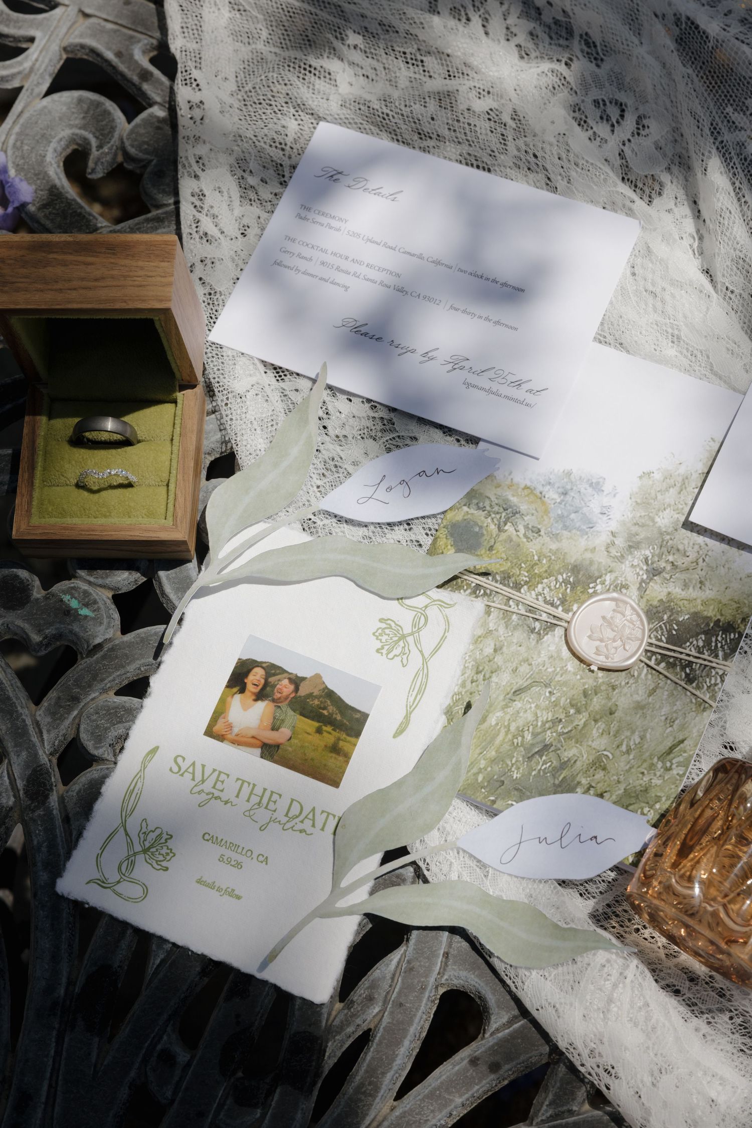 Elegant wedding stationery flat lay with save the date card, rings in wooden box, wax seal, and lace fabric.