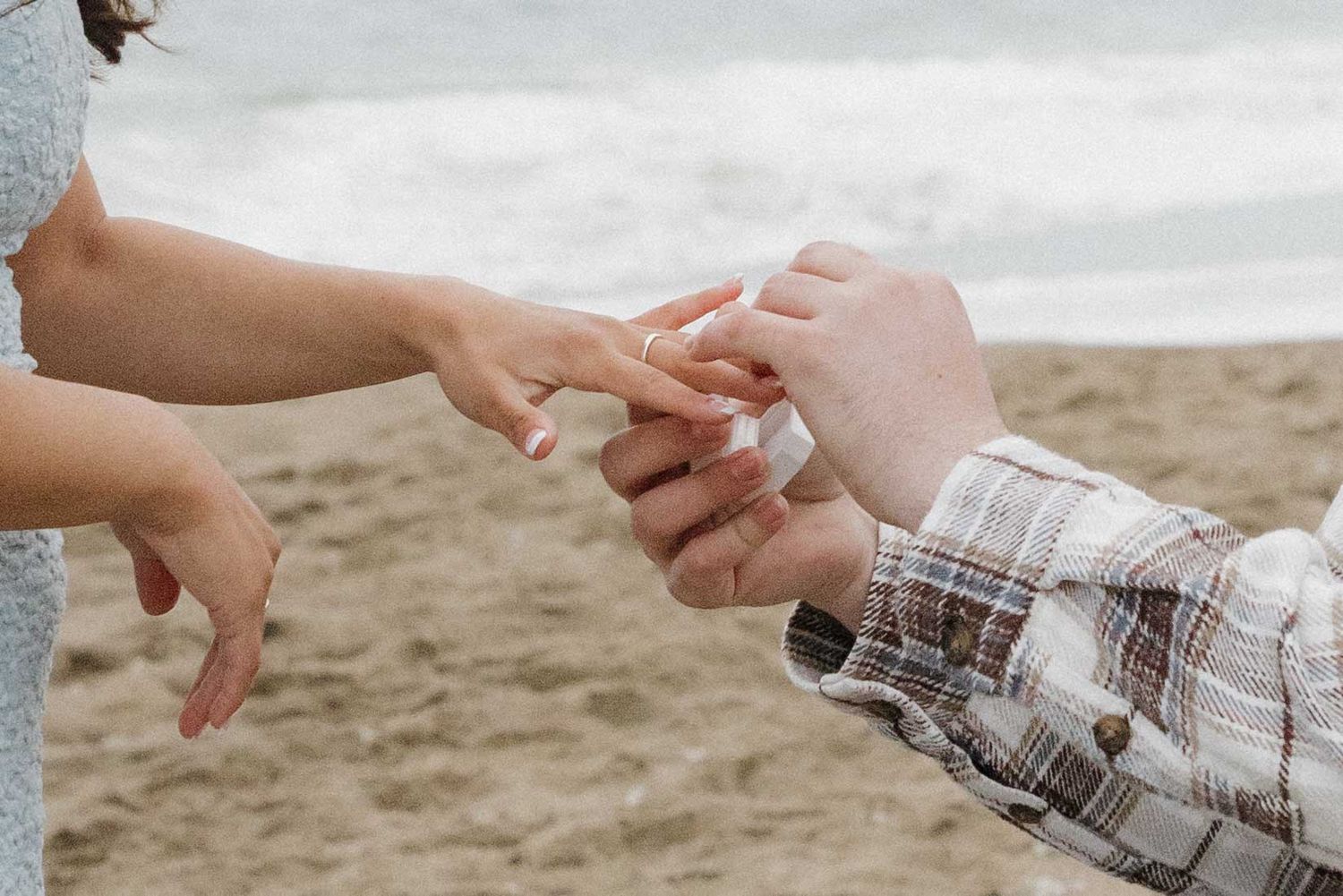 Two hands meet in a romantic moment on a sandy beach as one person places a ring on the other's finger.
