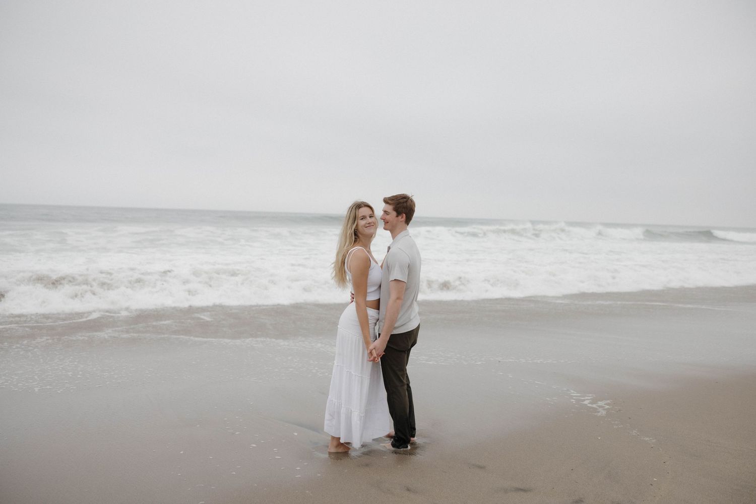Romantic beach scene with couple standing by ocean on overcast day.