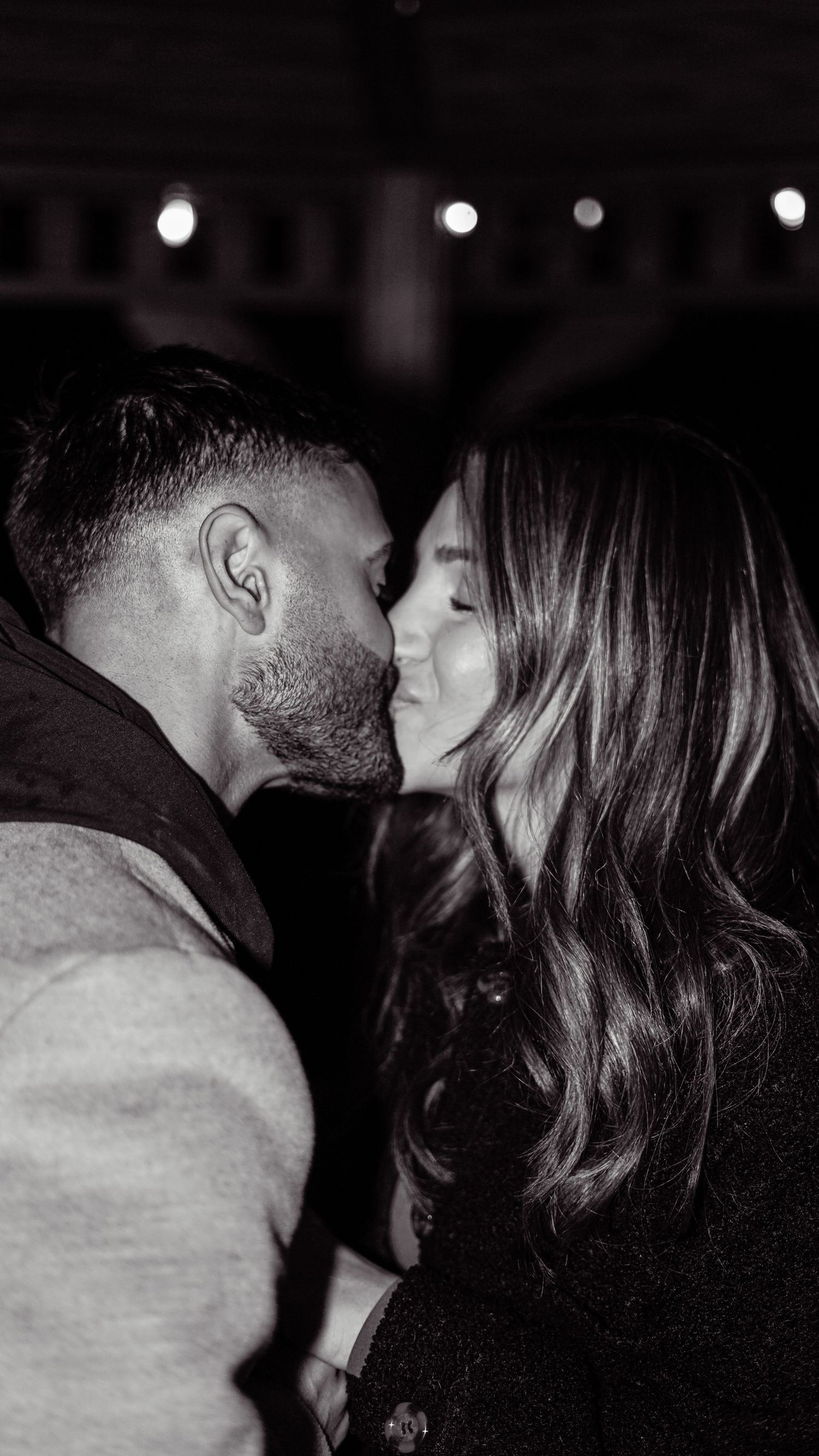 A romantic black and white photo captures an intimate moment between a couple sharing a tender kiss in low light.