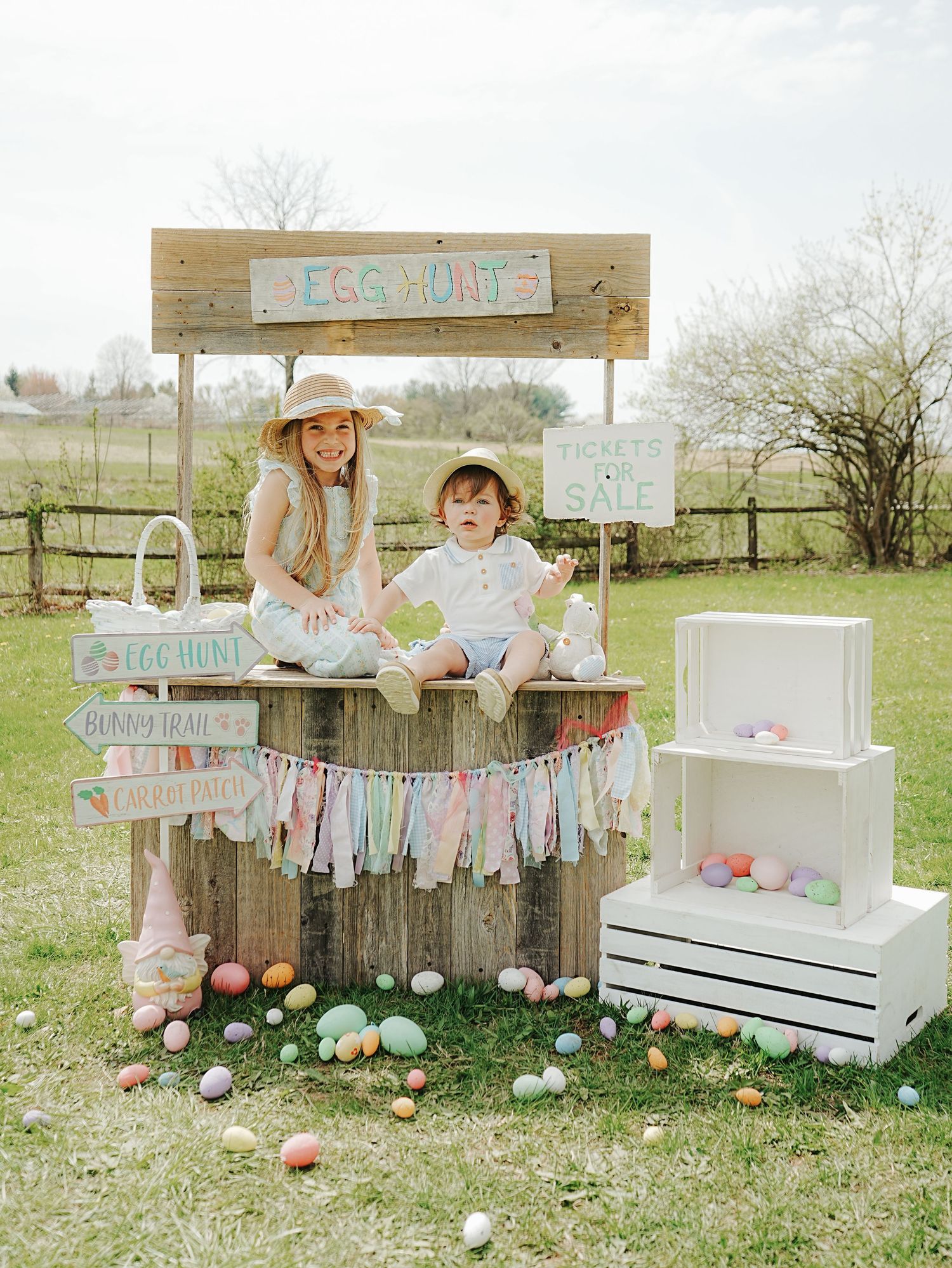A rustic Easter lemonade stand decorated with pastel bunting, colorful eggs, and white wooden crates in a spring garden setting.