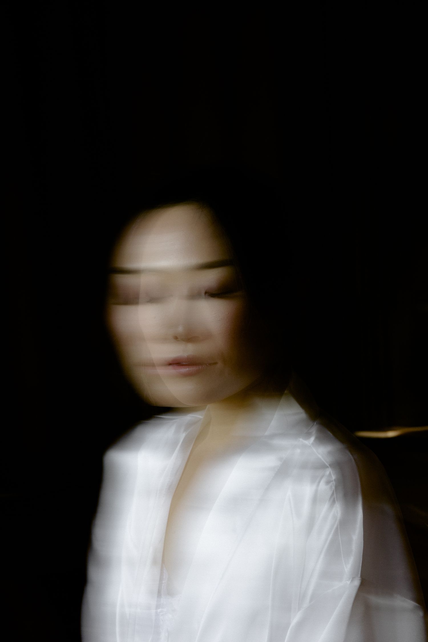Artistic motion blur portrait of someone in white clothing against dark background.
